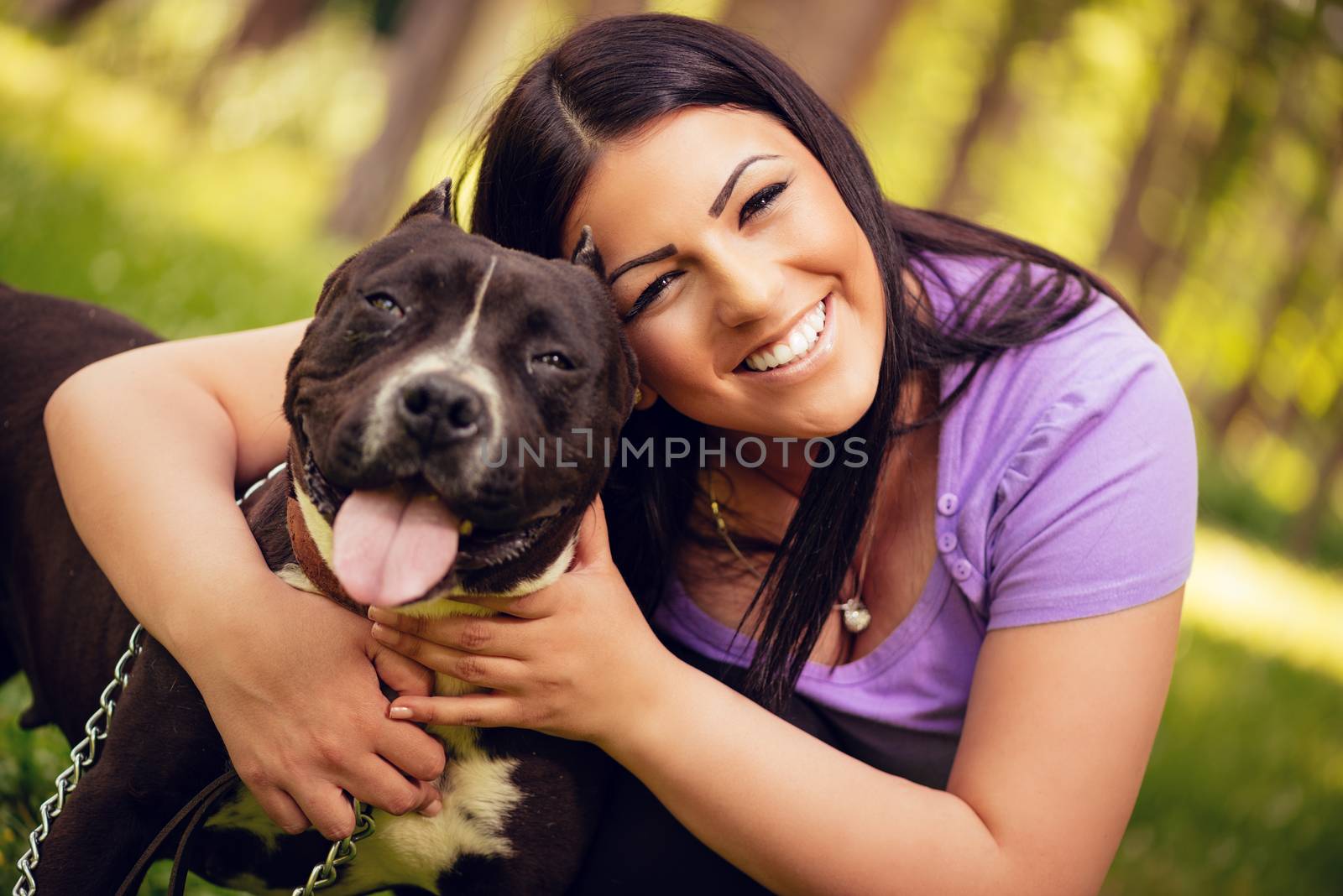 Portrait of a beautiful young woman hugging her cute stafford terrier in the park and enjoying. Looking at cemera.
