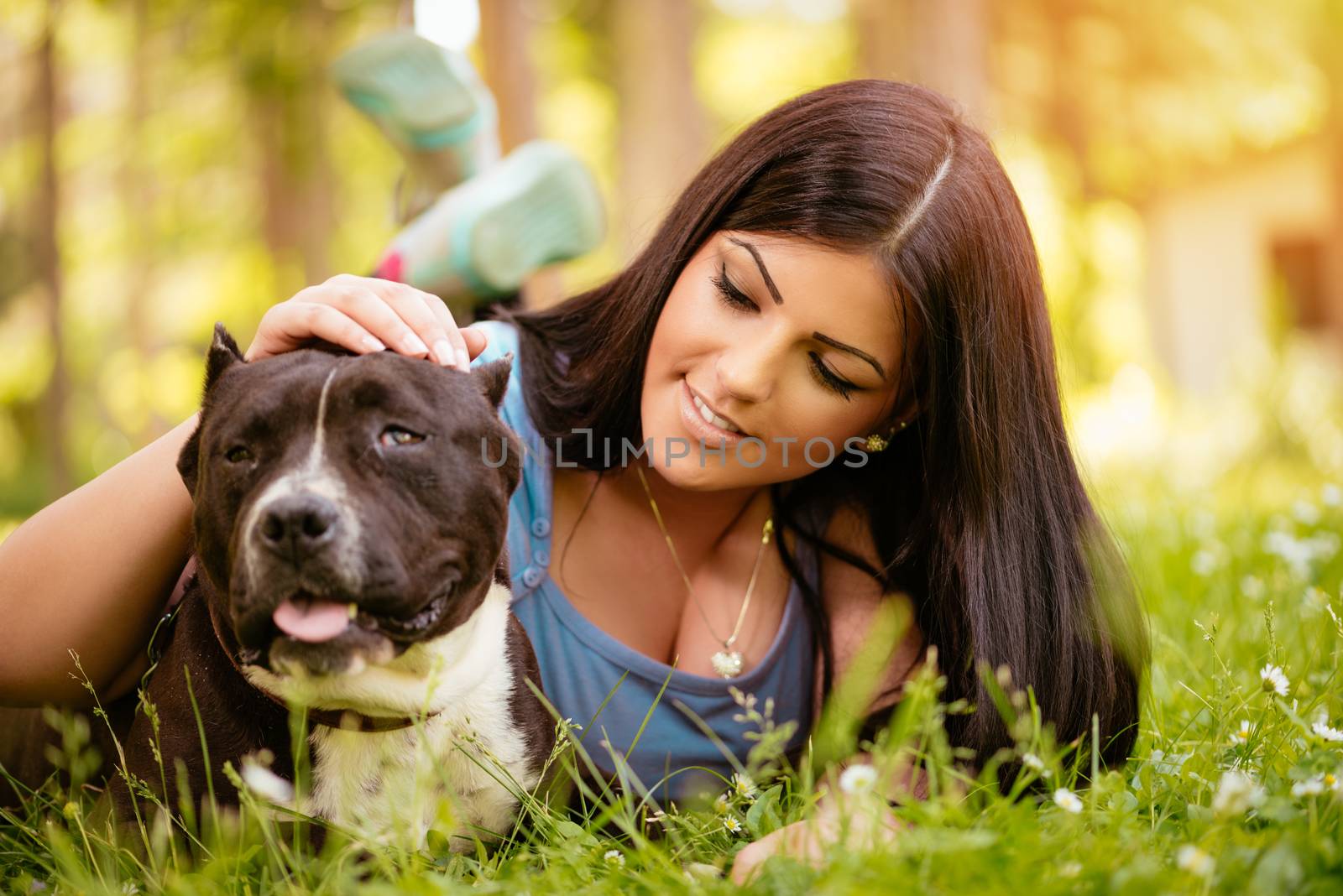 Beautiful young woman with her cute stafford terrier lying on grass in the park.
