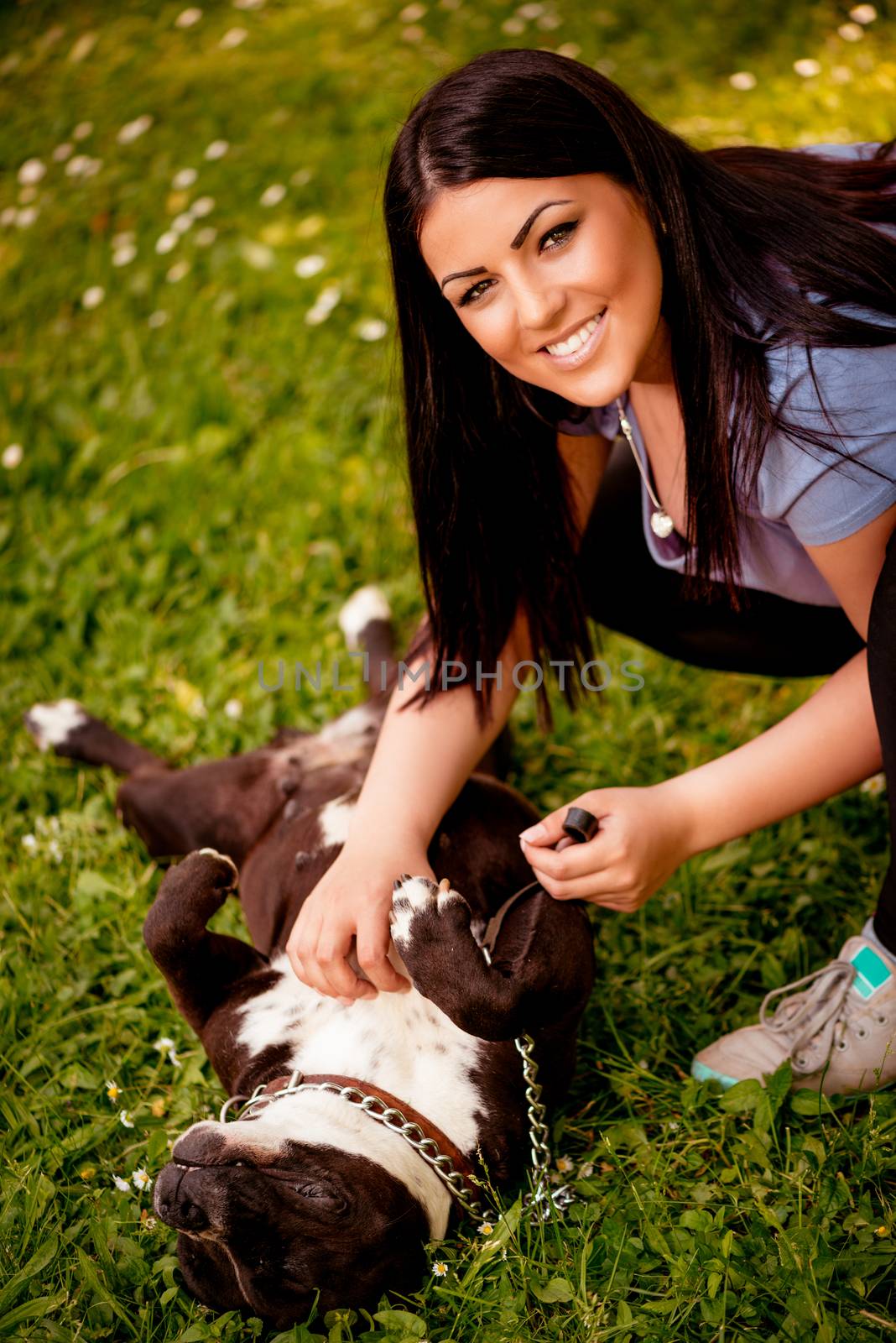 Beautiful young woman playing with her cute stafford terrier in the park.