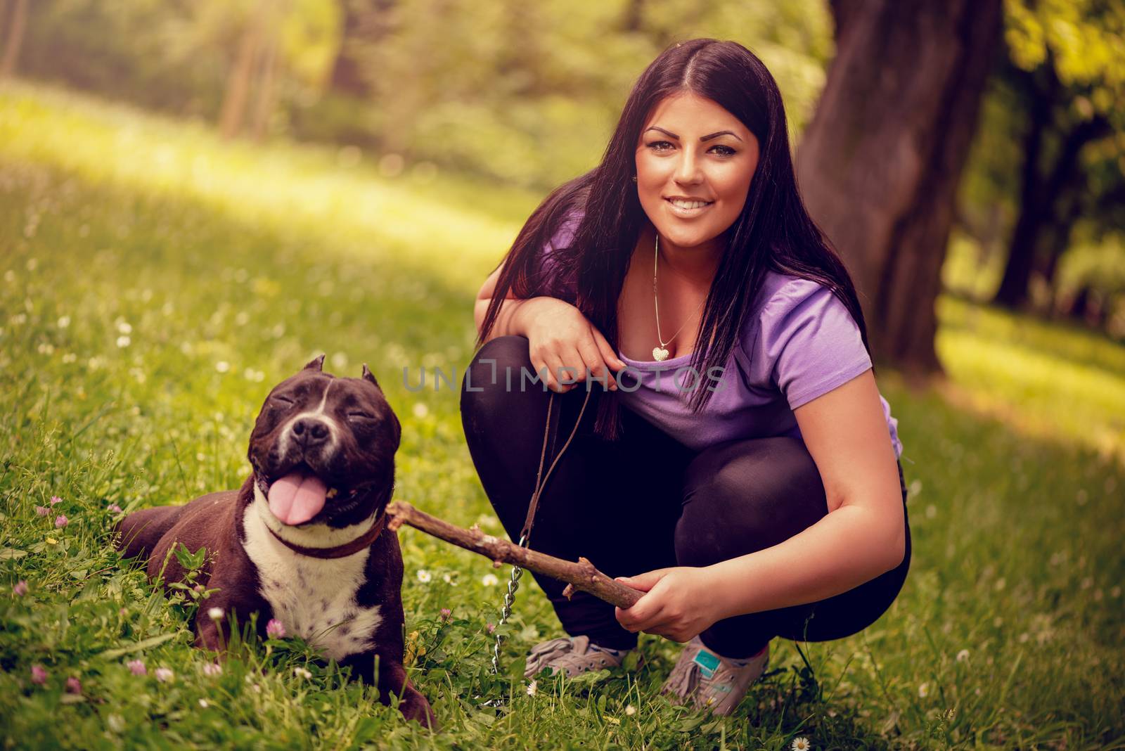 Beautiful young woman with her cute stafford terrier in the park. Looking at camera.