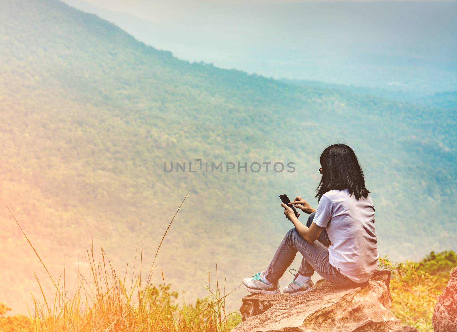 Young Asian woman sit on the rock at the cliff and using smart phone message to her friends while on vacation at the national park. Adventure travel and communication concept by Fahroni