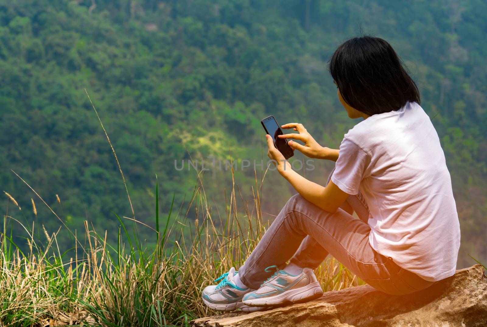 Young Asian woman sit on the rock at the cliff and using smart phone message to her friends while on vacation at the national park. Adventure travel and communication concept by Fahroni