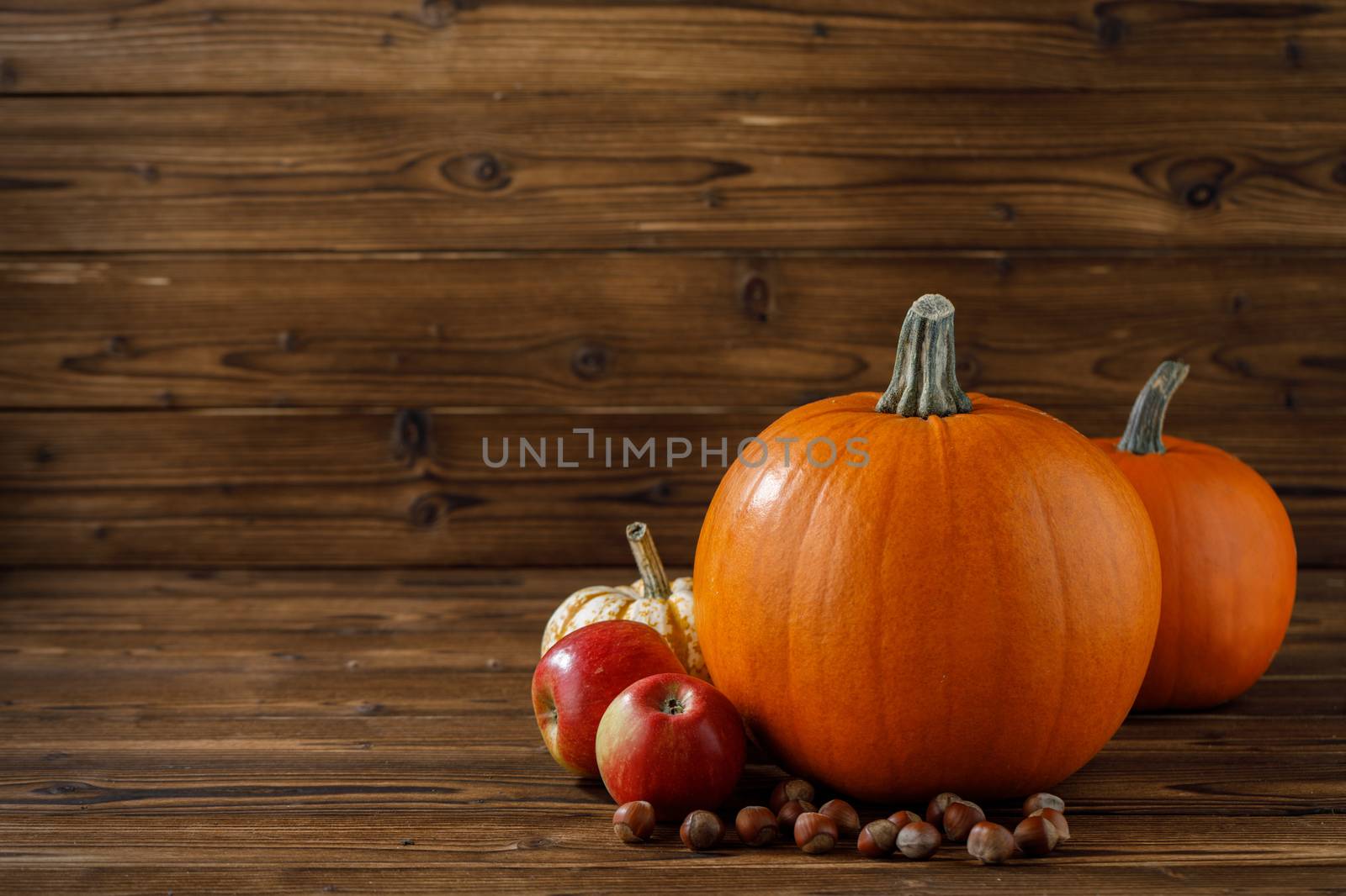 Autumn harvest still life with pumpkins, apples and hazelnuts on wooden background