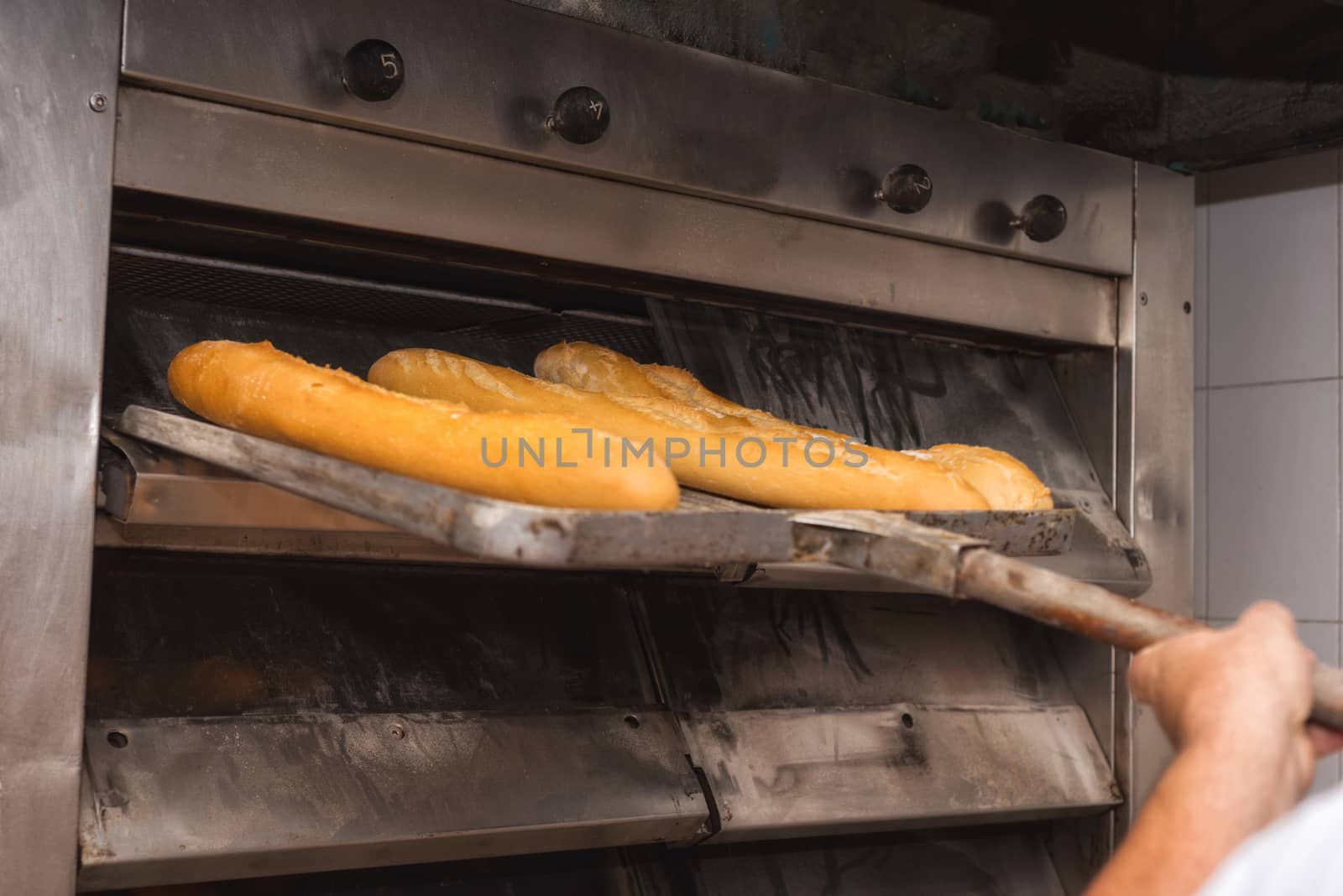 Baker taking out fresh baked bread from the industrial oven by HERRAEZ