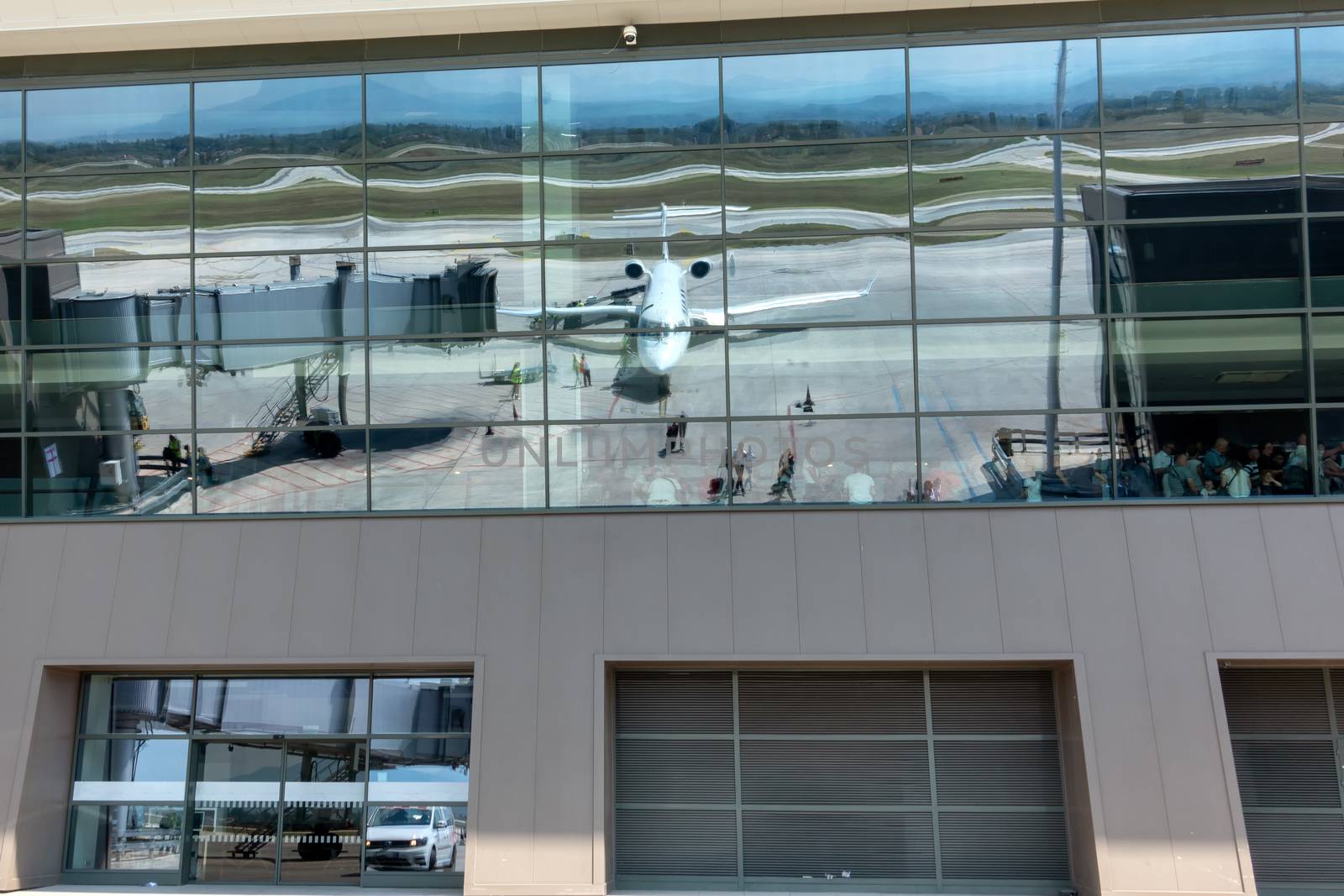 Reflection of passenger jet airplane in glass windows of airport terminal building where other passengers are waiting to board their flights