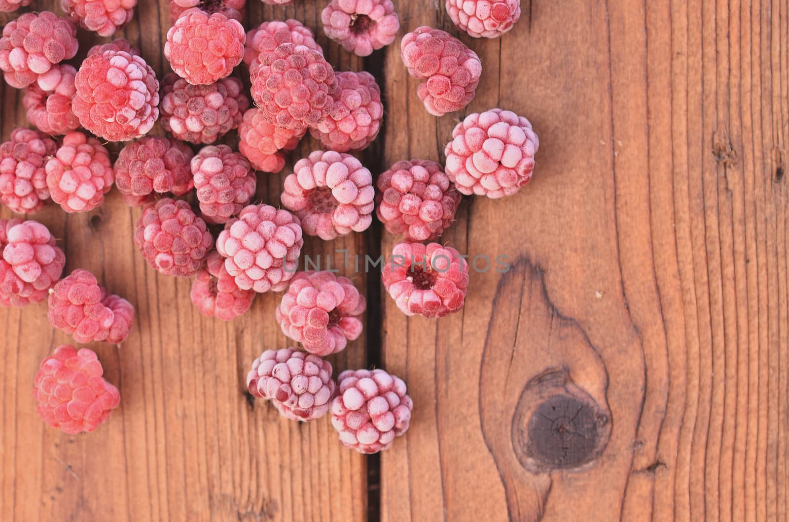 Covered with frozen raspberries, they are lying on the wooden background from the top left