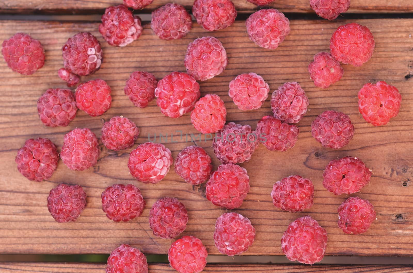 On a wooden background, raspberries are scattered, a photo from above