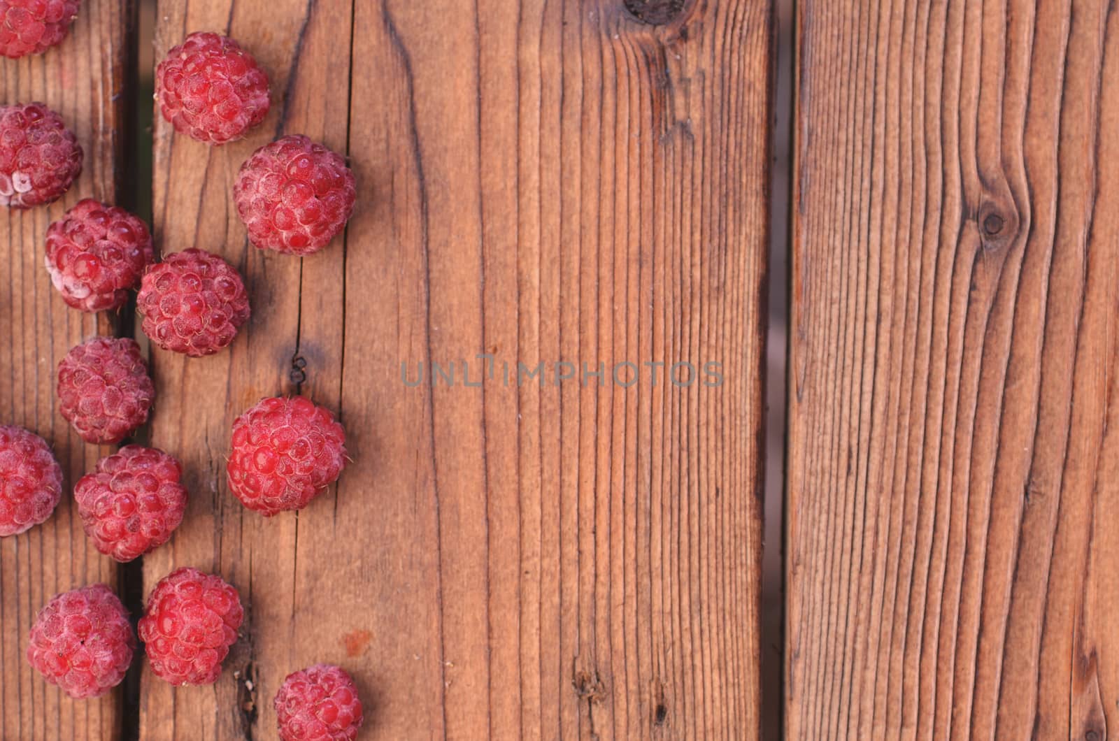 On a wooden background, raspberry is spread out on the left, a photo from above