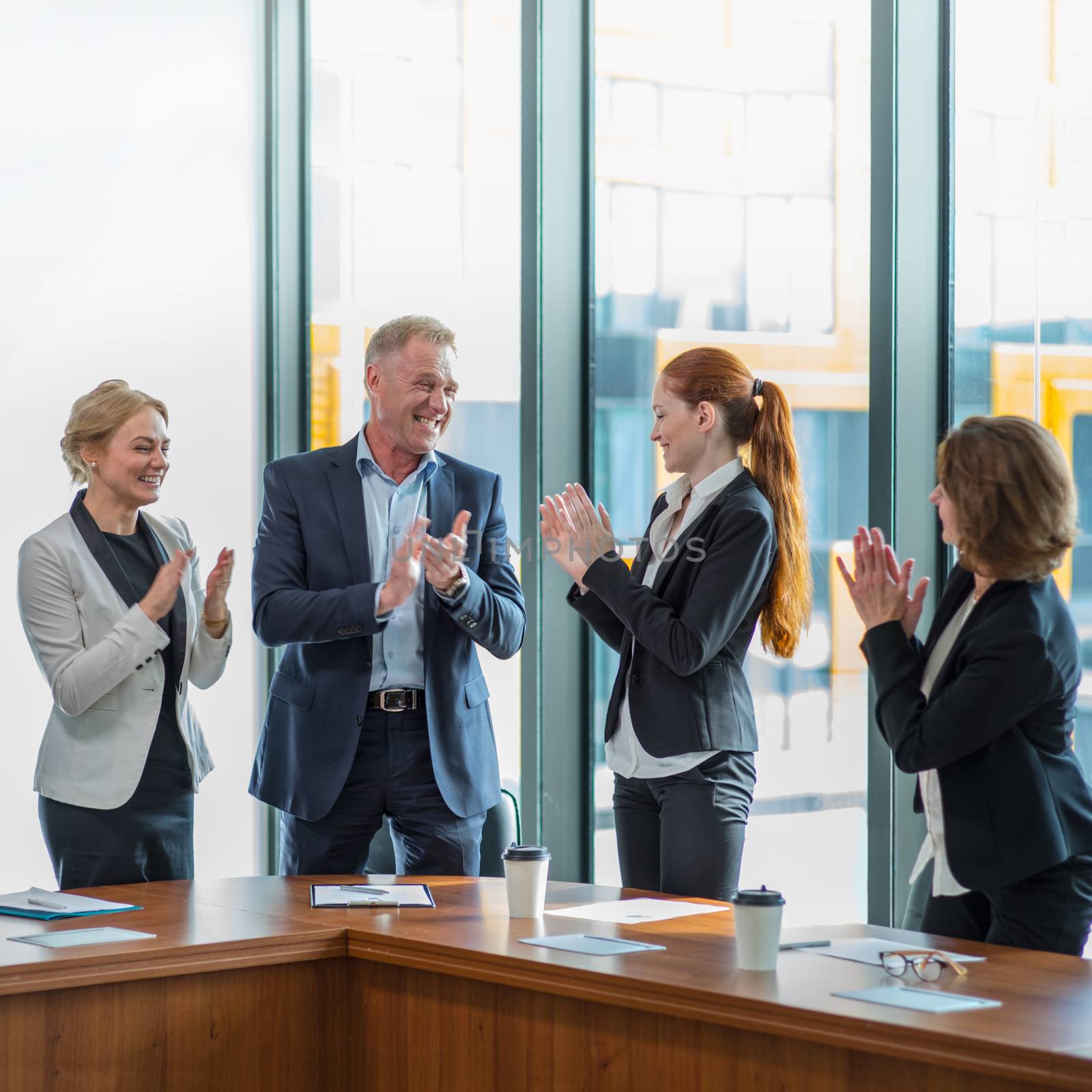 Business people group clapping and smiling in office standing around meeting table