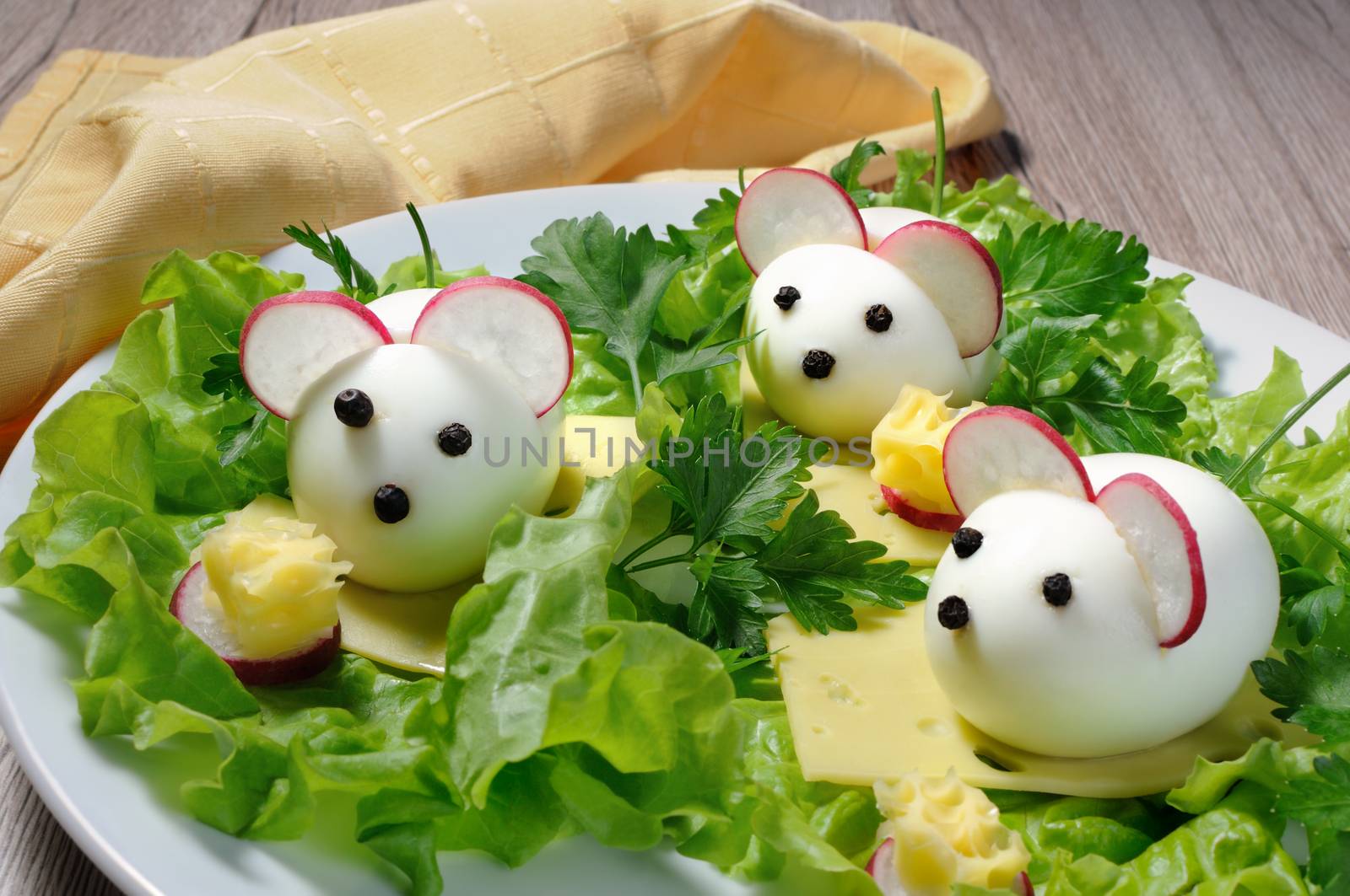 Serving a festive children's snack, boiled eggs in the form of mice in lettuce leaves and cheese cubes