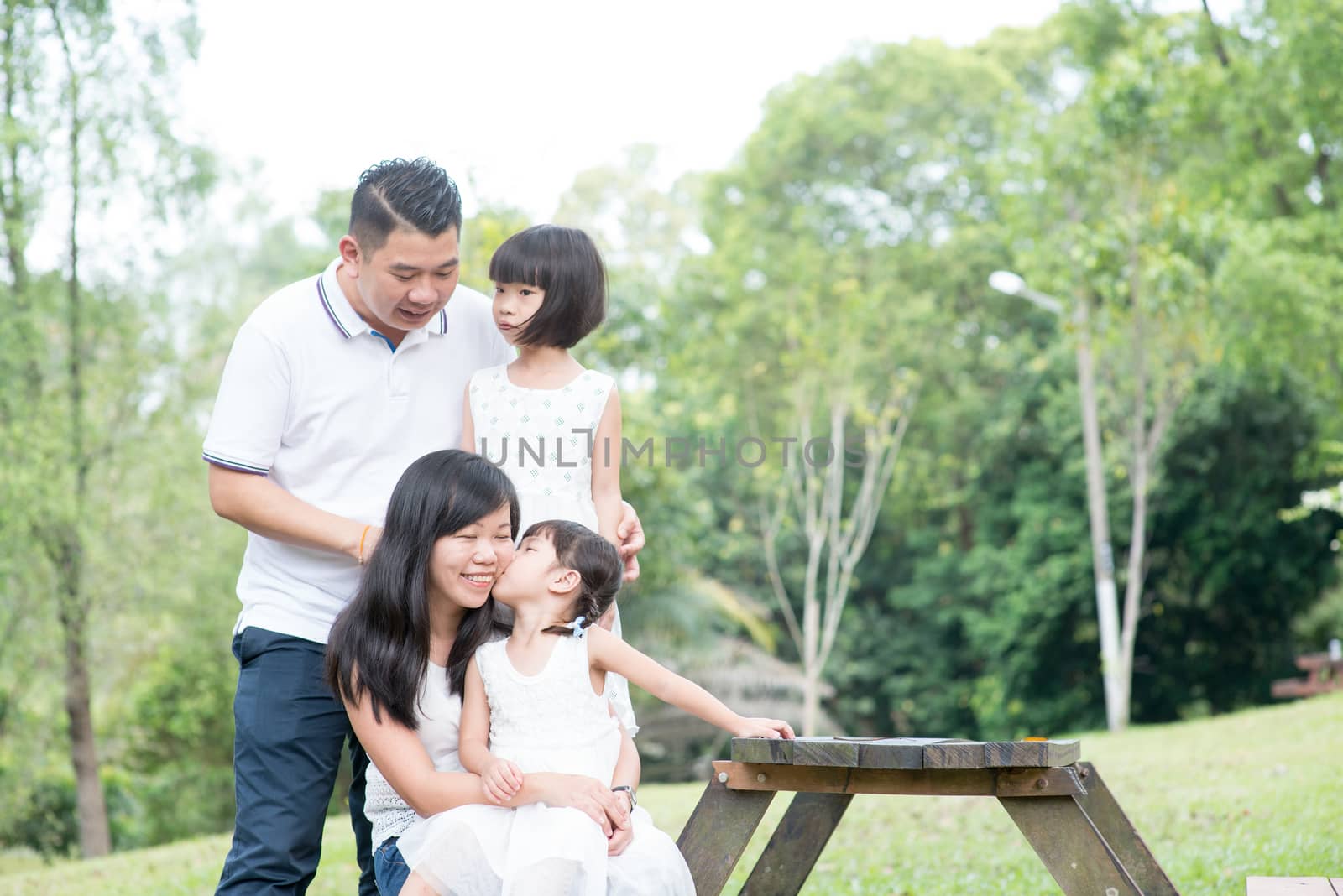 Asian family portrait. Parents and children having fun at outdoor park. Empty space on wooden table.