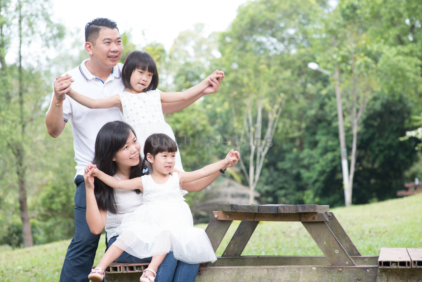 Asian family portrait. Parents and children playing at outdoor park. Empty space on wooden table.