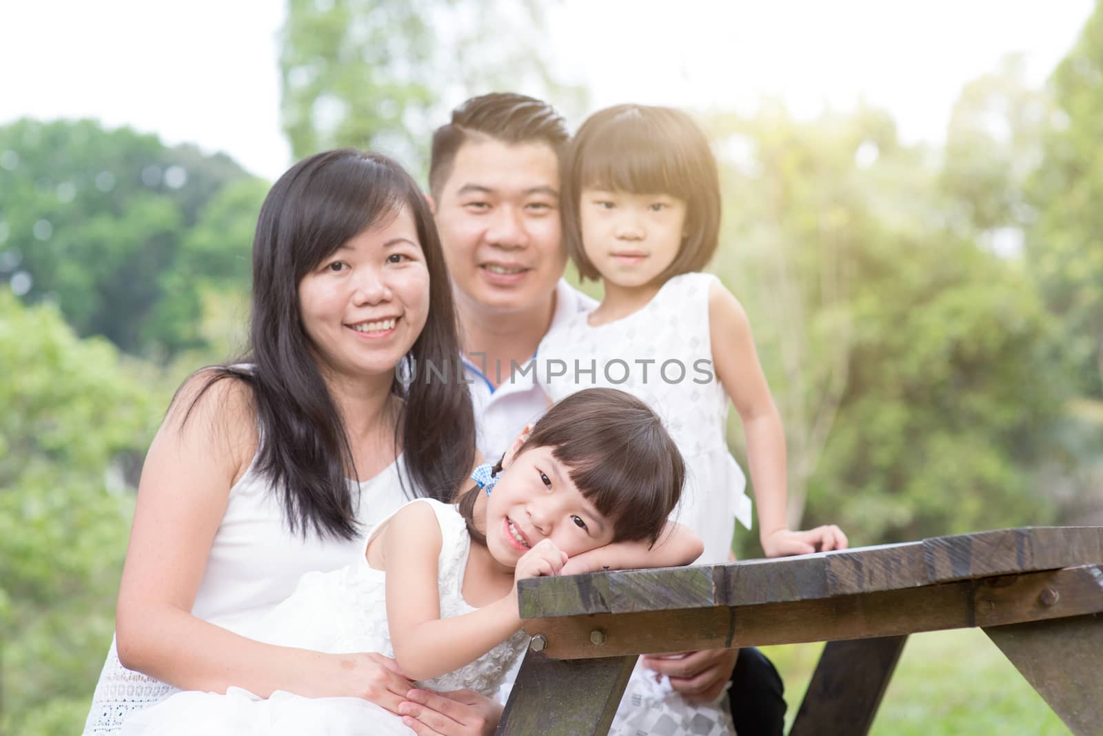 Asian family portrait. Parents and children sitting at outdoor park. Blank space on wooden table.