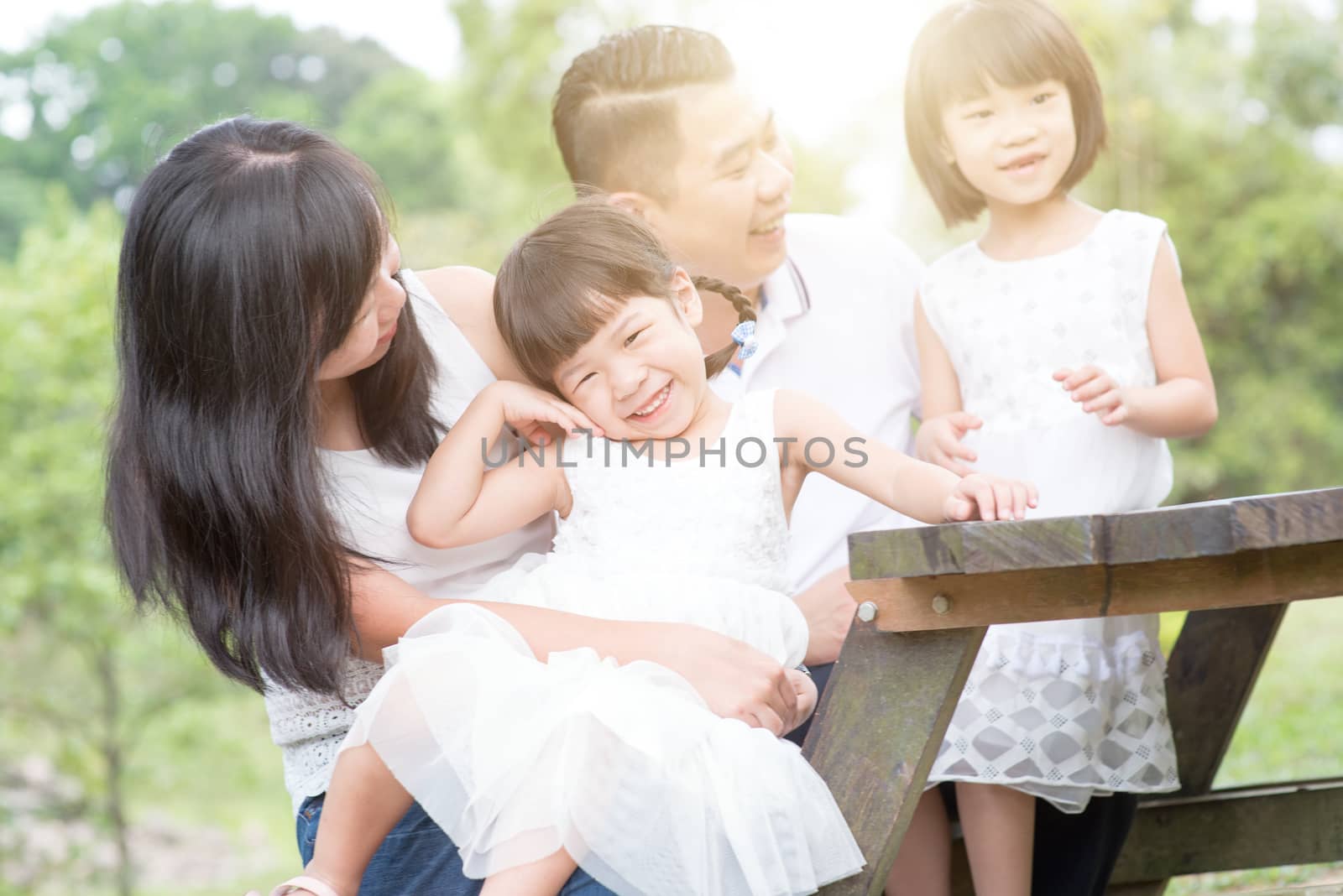 Asian family portrait. Parents and children at outdoor park. Blank space on wooden table.