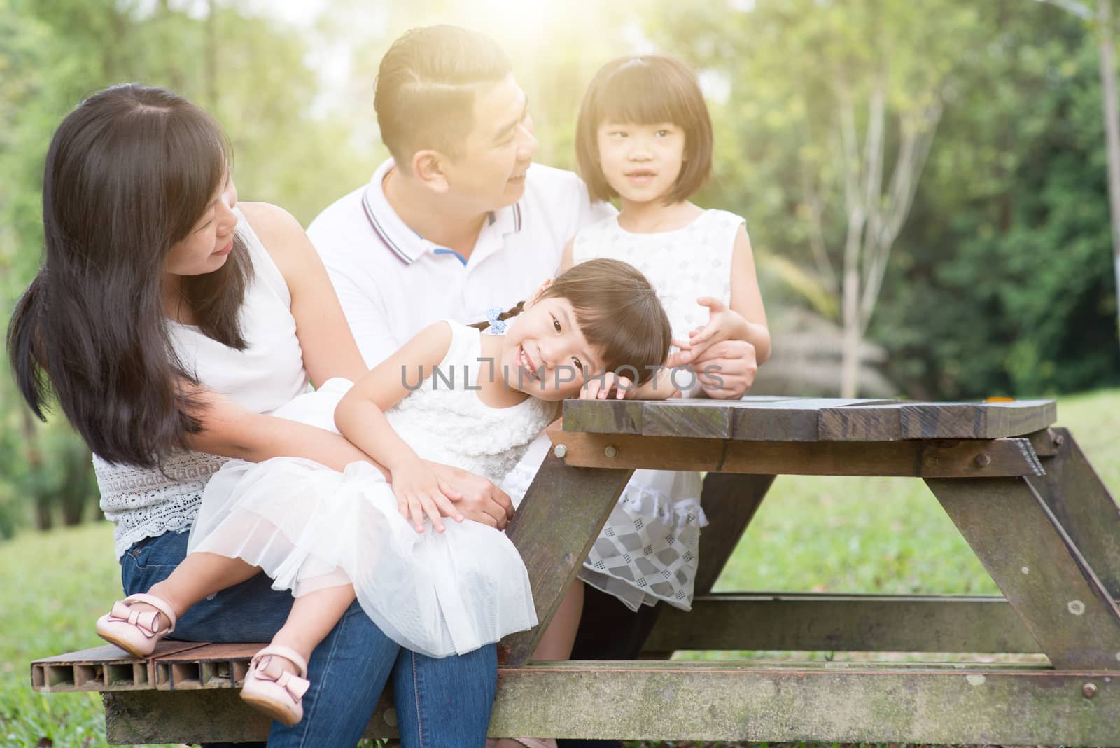 Asian family portrait. Parents and children having fun at outdoor park. Blank space on wooden table.
