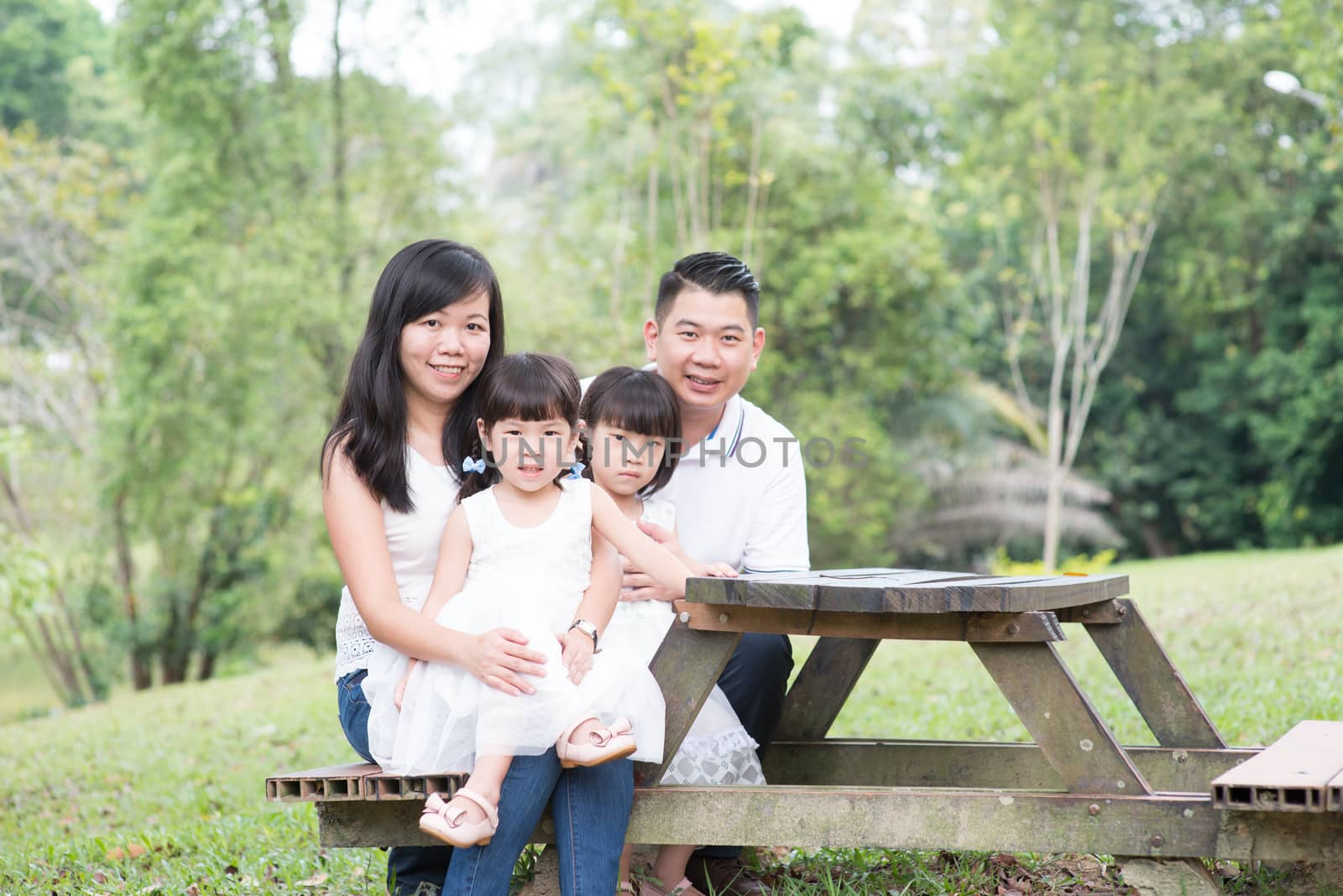 Asian family portrait. Parents and children sitting at outdoor park. Empty space on wooden table.