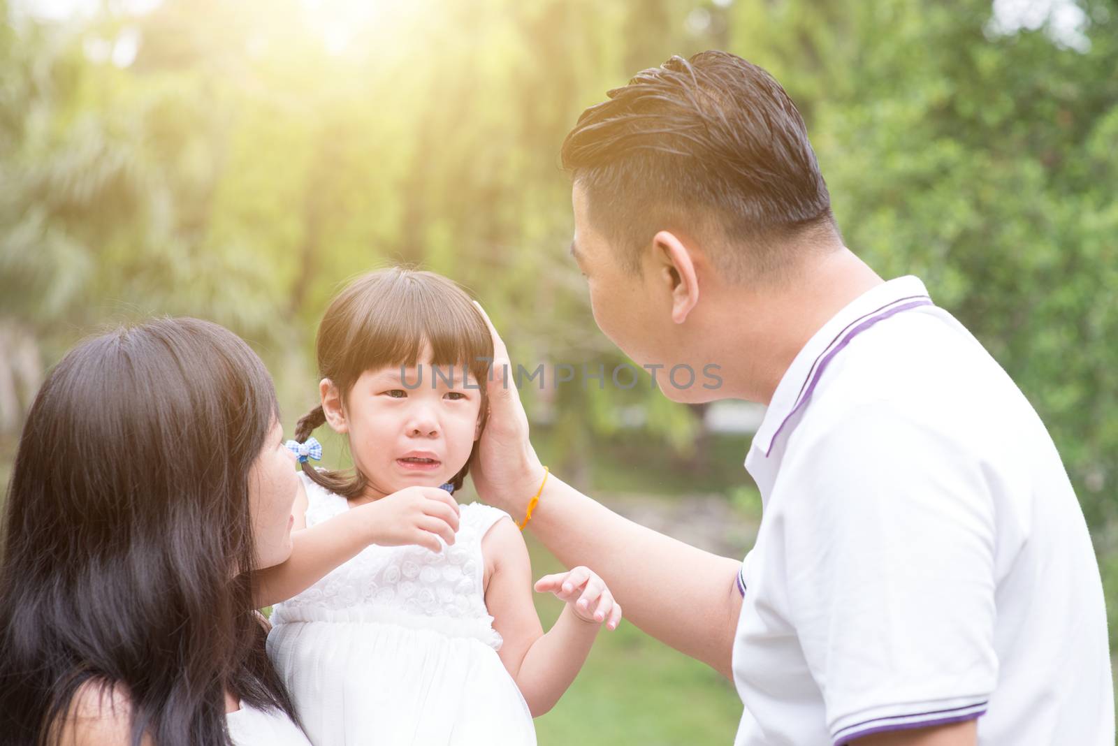 Parents comfort crying daughter at outdoor garden park. Asian family outdoors portrait.