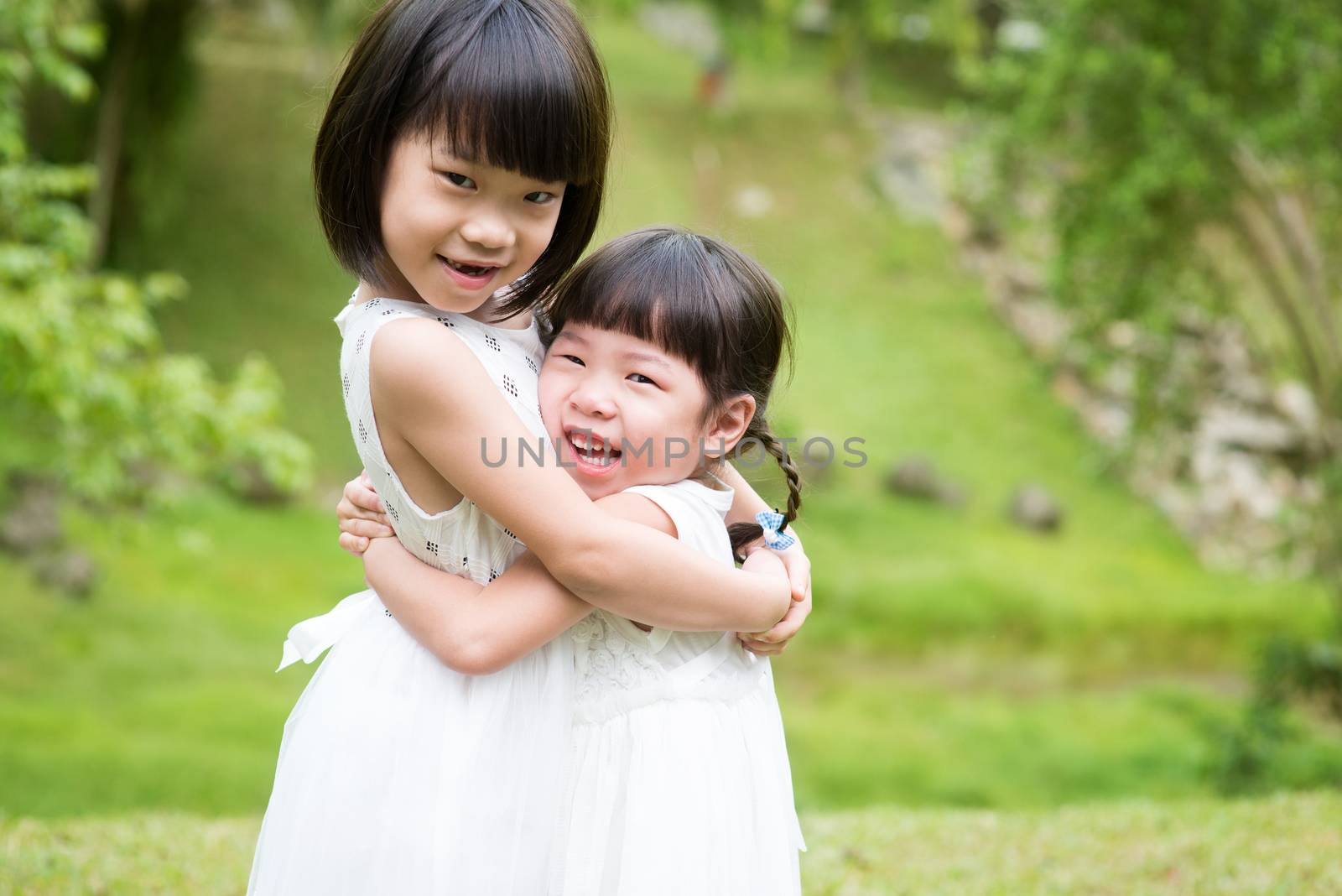 Cute sisters playing and hugging at garden park. Asian family outdoors portrait.