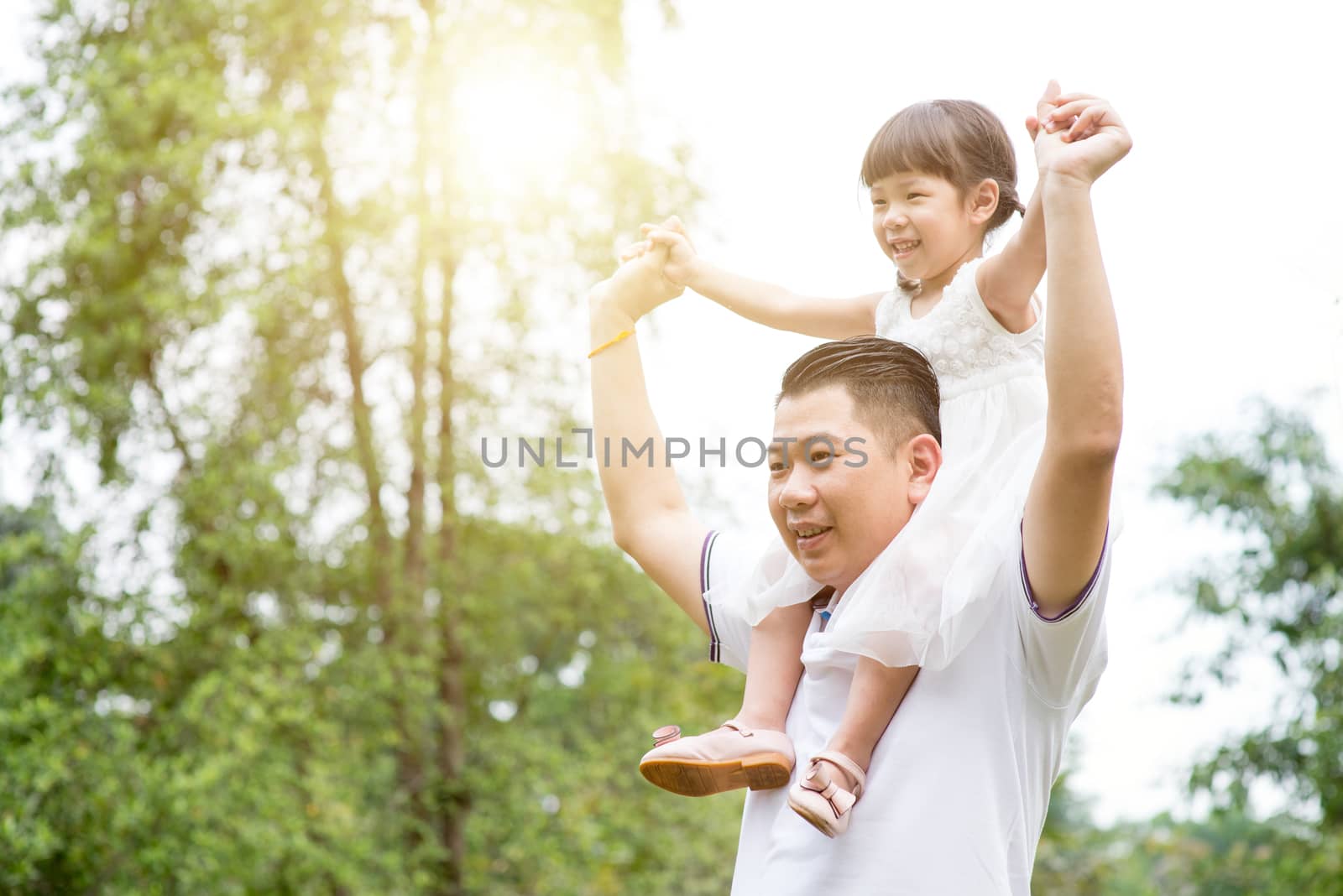 Asian family outdoors portrait. Father piggyback daughter at green park. 