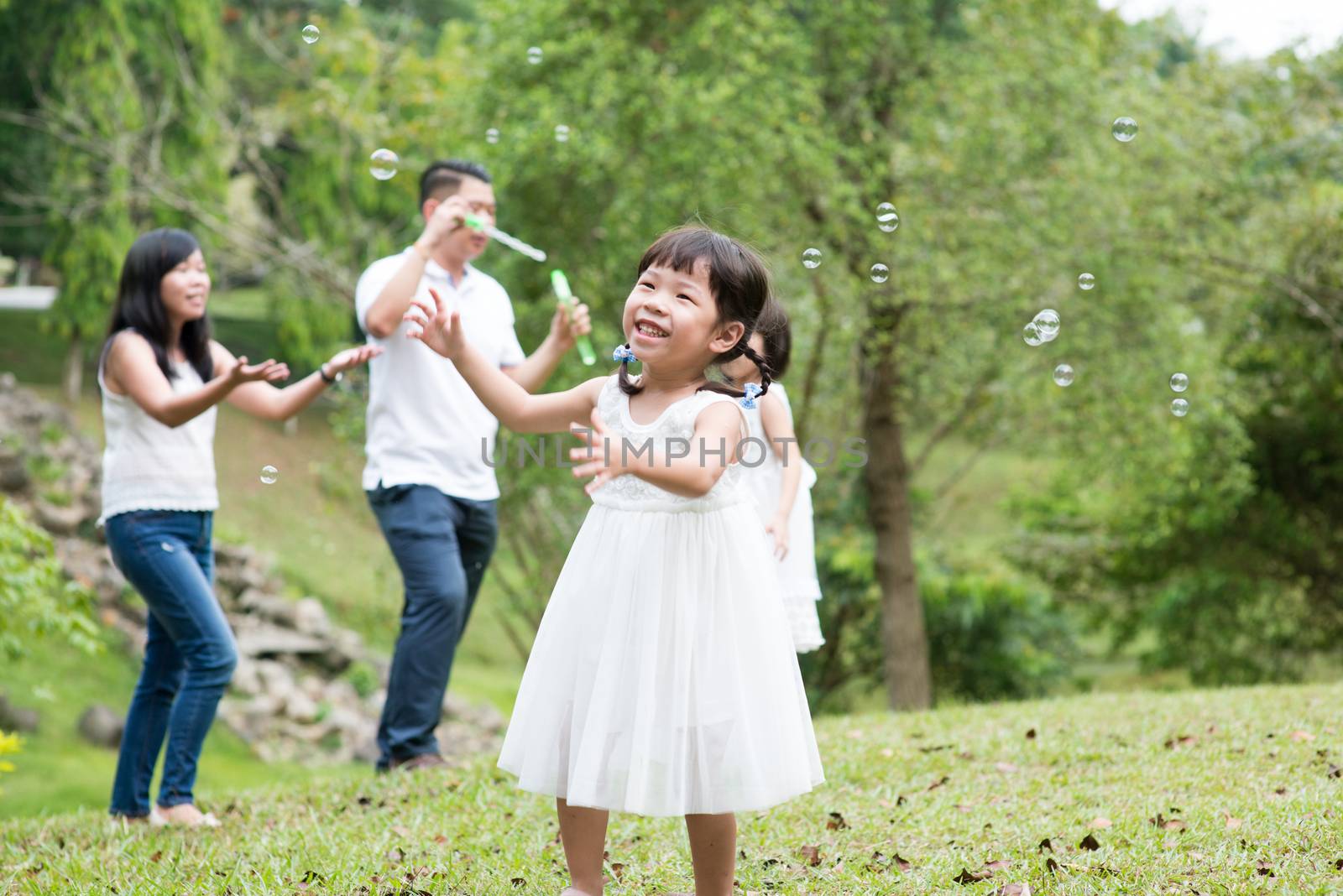 Parents and children blowing soap bubbles at park. Asian family outdoors activity.