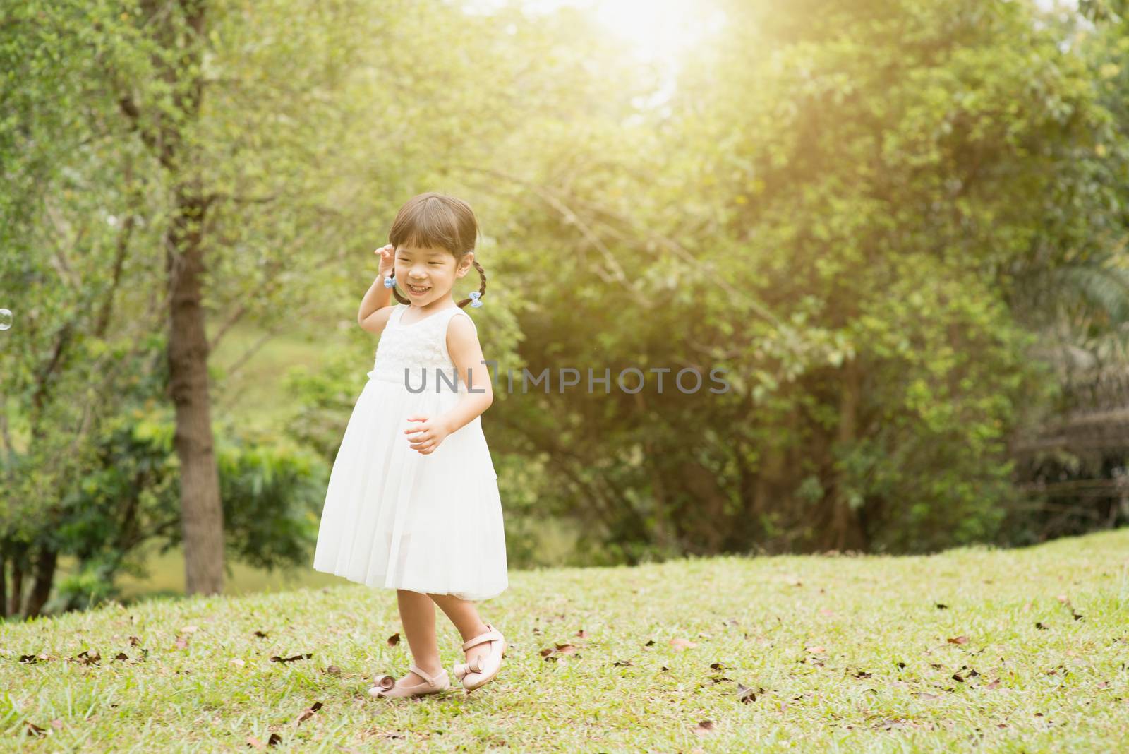 Happy little girl playing at green park. Asian family outdoors portrait.