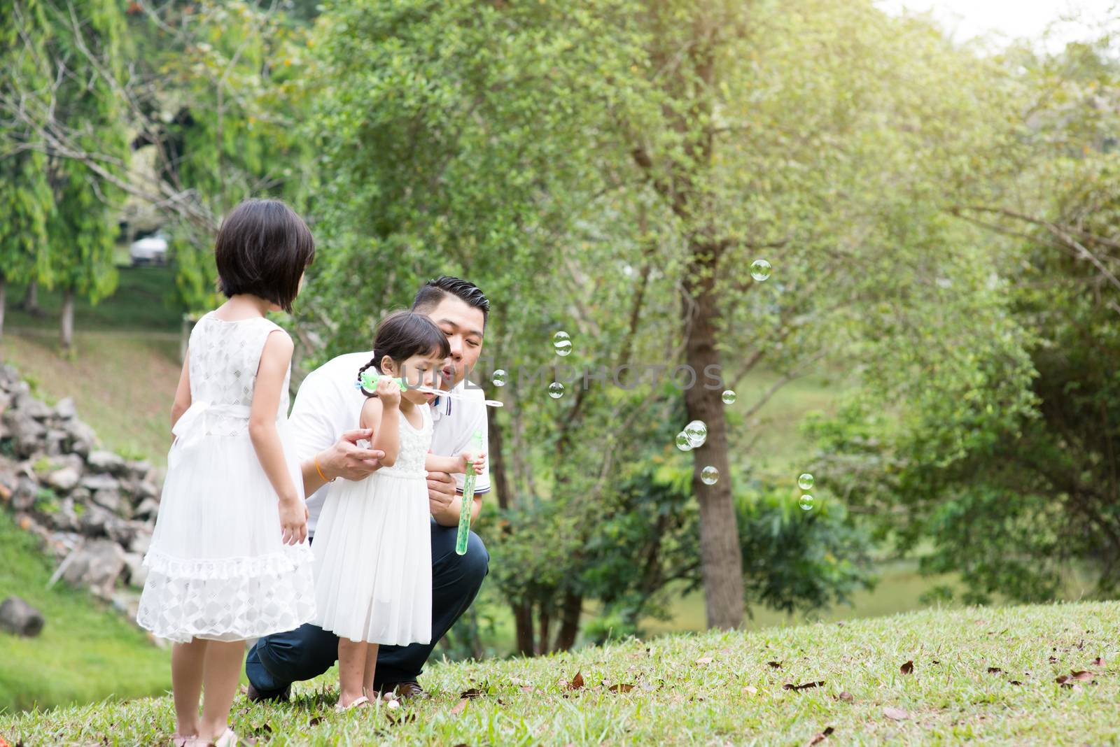 Happy Asian family blowing soap bubbles at park by szefei