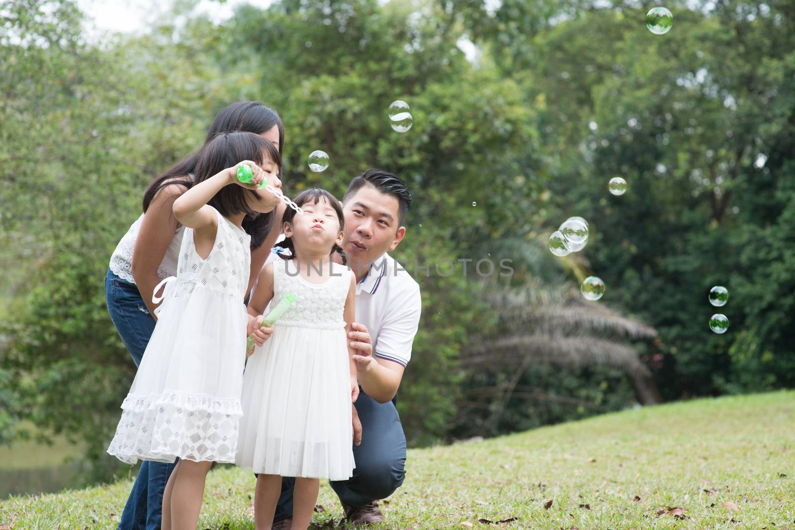 Asian family outdoors activity. Parents and children blowing soap bubbles at park. 