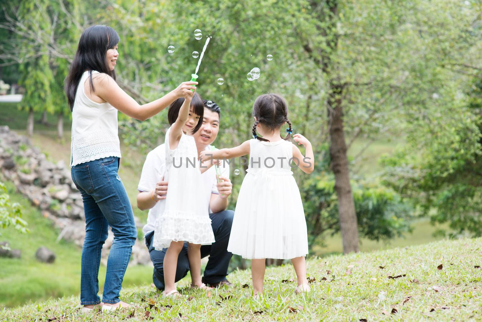 Asian family blowing soap bubbles at park by szefei