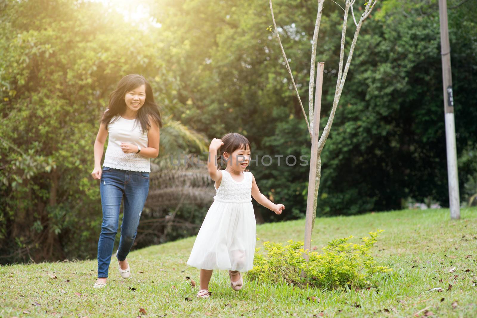 Mother and little girl playing and running at green park. Asian family outdoors activity.