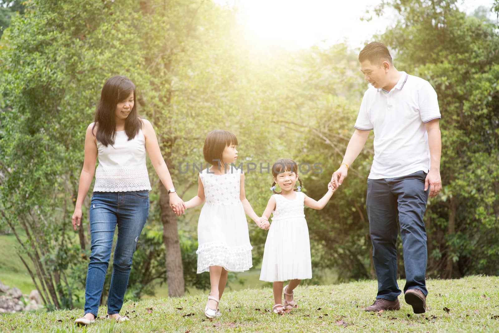 Asian family outdoors. Parents and children holding hands and walking at green park. 