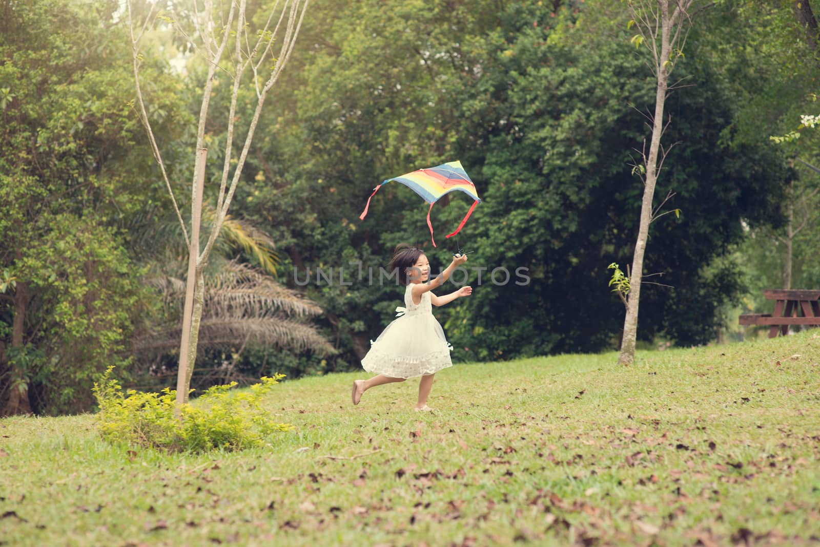 Asian family outdoors activity. Little girl running and flying kite at garden park. 