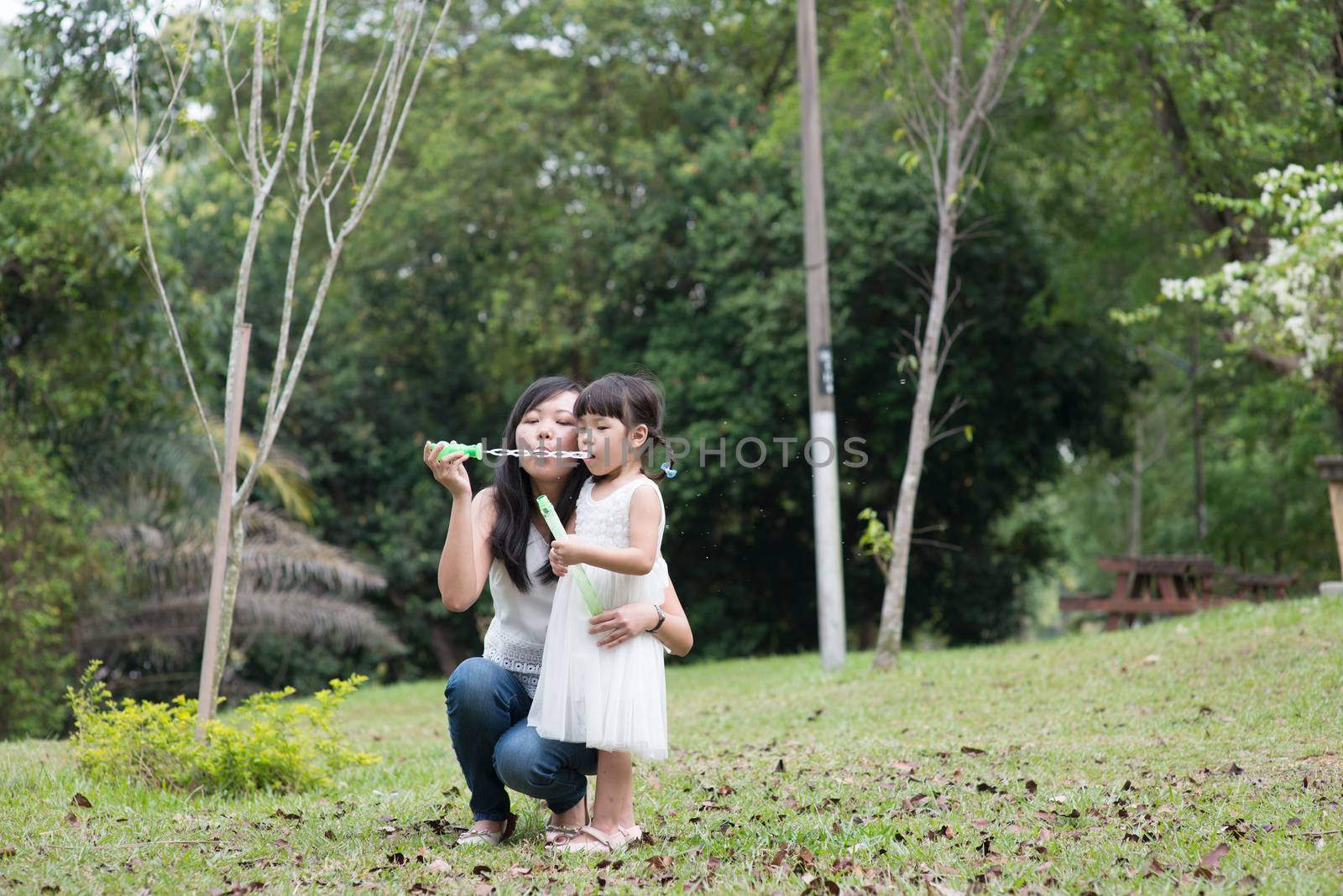 Asian family outdoors activity. Mother and daughter blowing soap bubbles at garden park. 