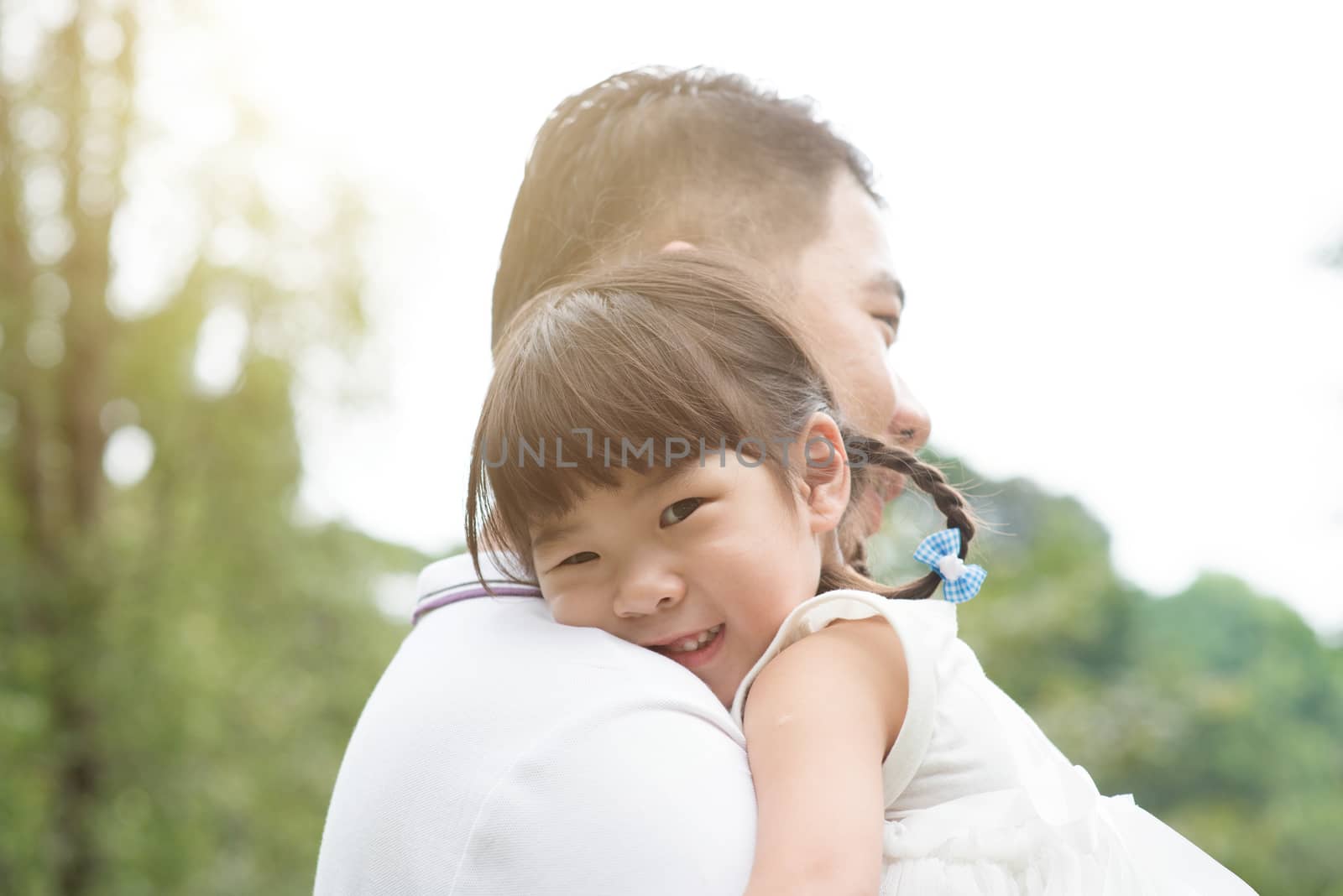 Asian family outdoors portrait. Father holding daughter at green park. 