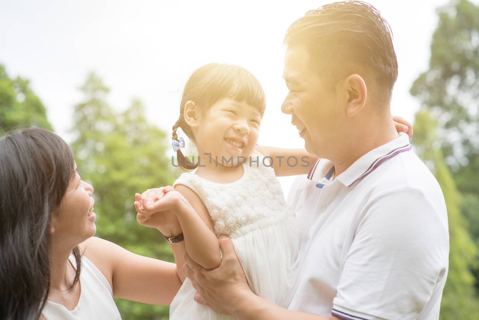 Happy parents and child bonding at green park. Asian family outdoors activity.