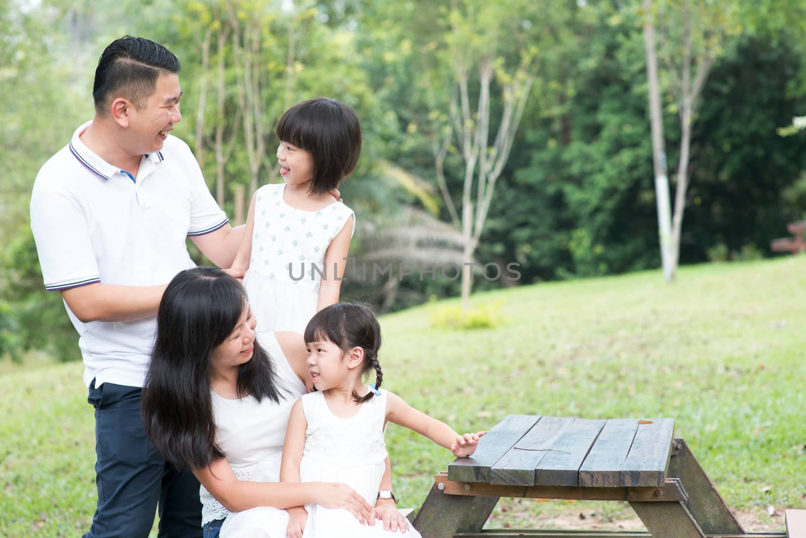 Asian family portrait. Parents and children bonding at outdoor park. Empty space on wooden table.
