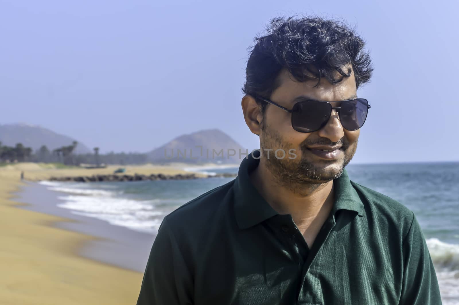 Portrait of elegant Indian man in formal t shirt and sunglasses outdoors, sea backgrounds with copy space.