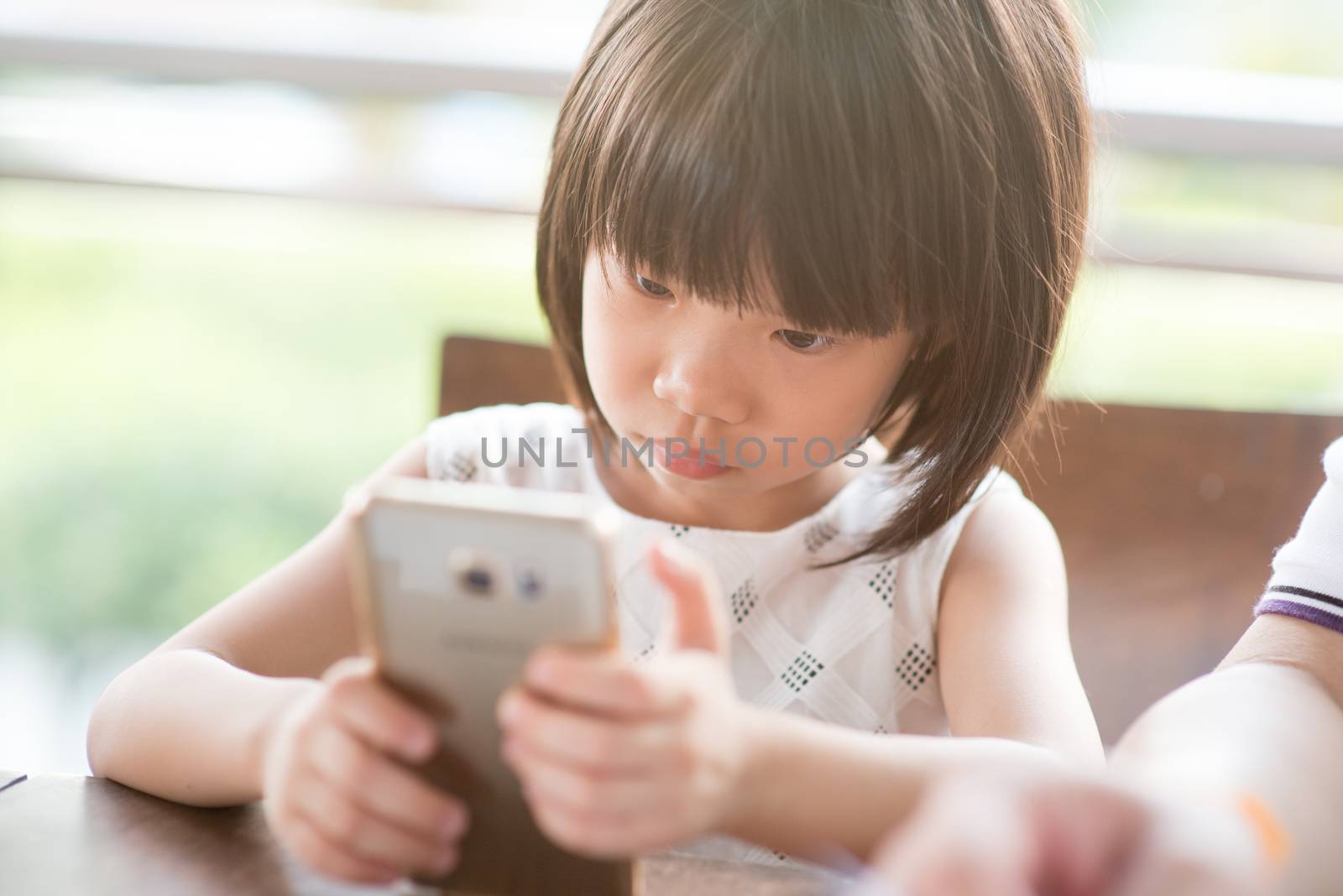 Asian child playing smart phone at cafe. Natural light outdoor lifestyle.