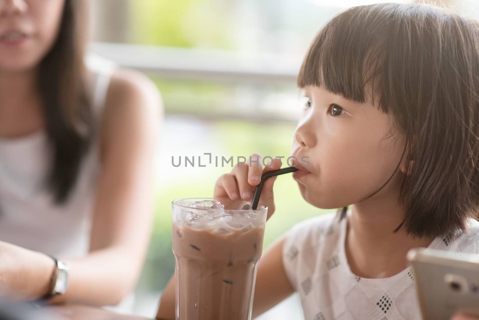 Asian child drinking iced chocolate at cafe. Natural light outdoor lifestyle.