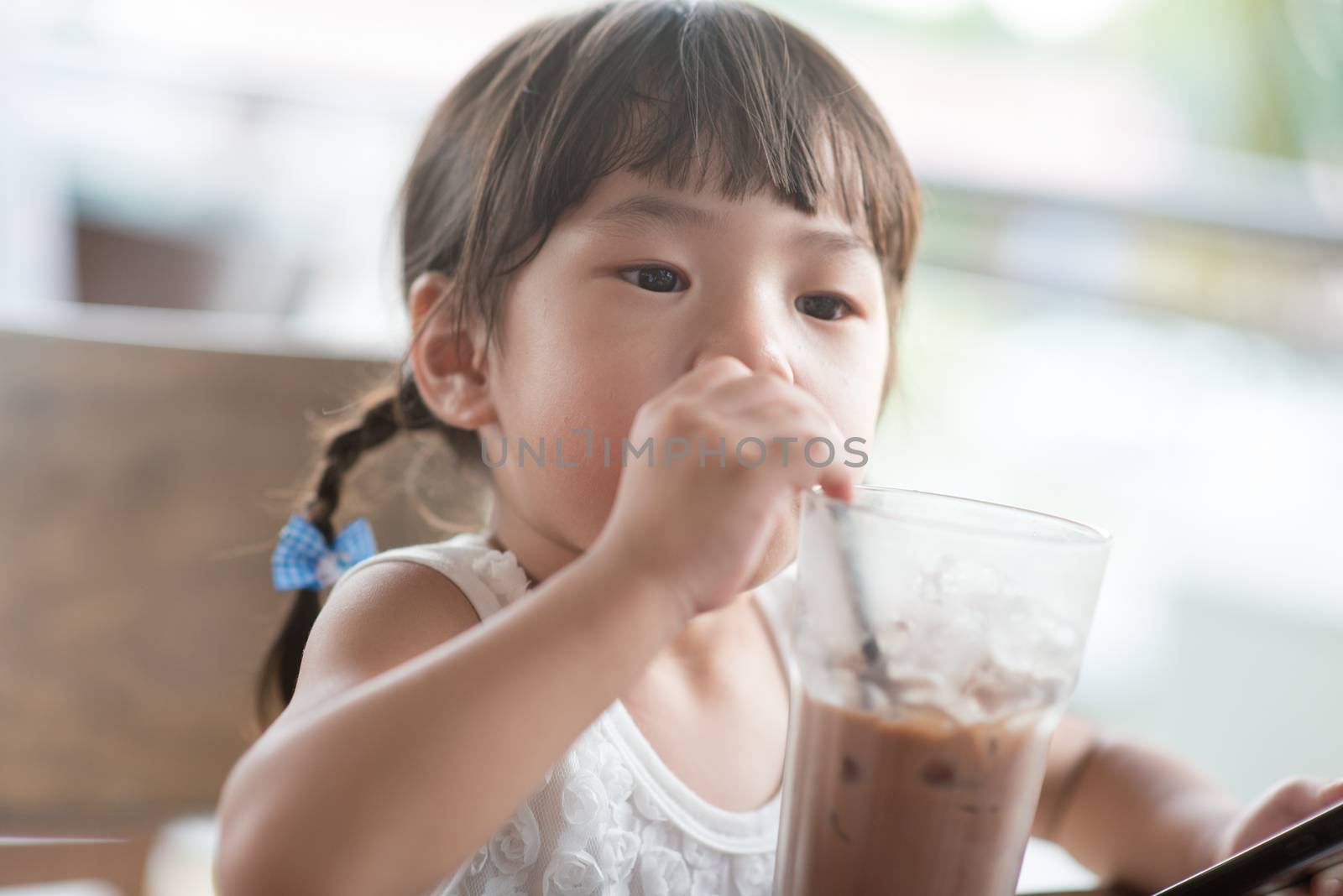 Little Asian girl drinking iced chocolate at cafe. Natural light outdoor lifestyle.