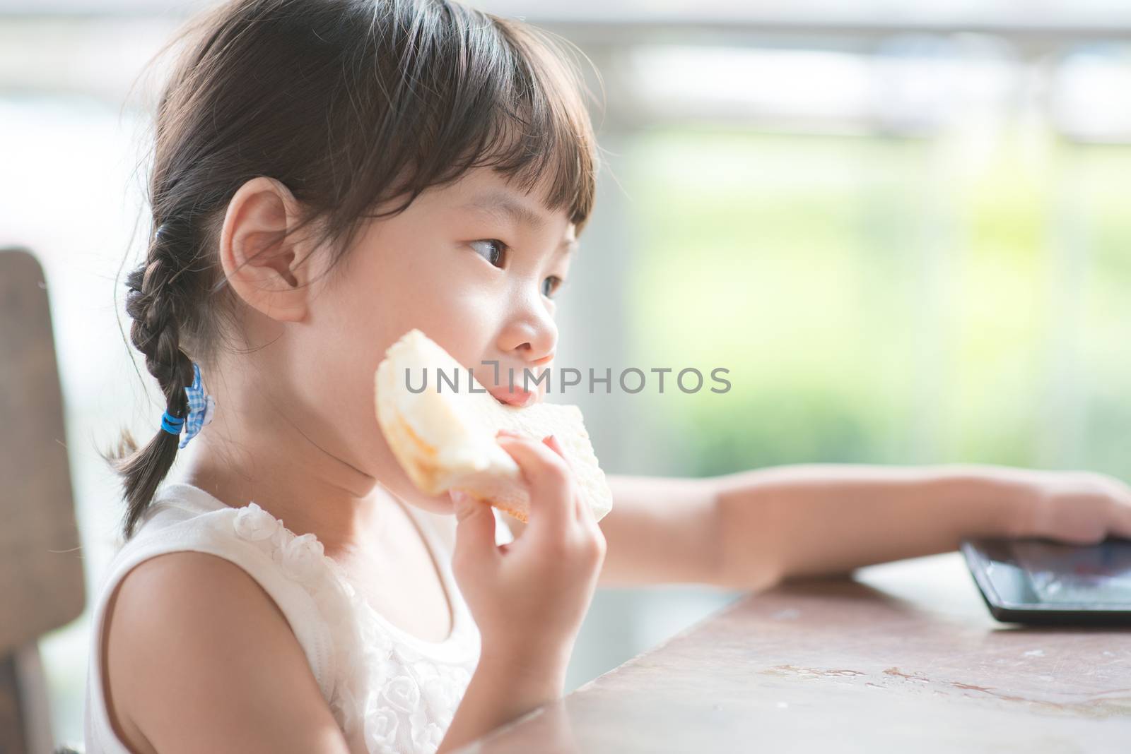 Little Asian child eating butter toast at cafe. Outdoor family lifestyle with natural light.