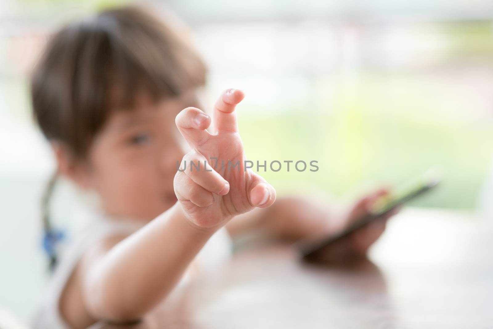 Little playful Asian girl playing smart phone at cafe. Natural light outdoor lifestyle.