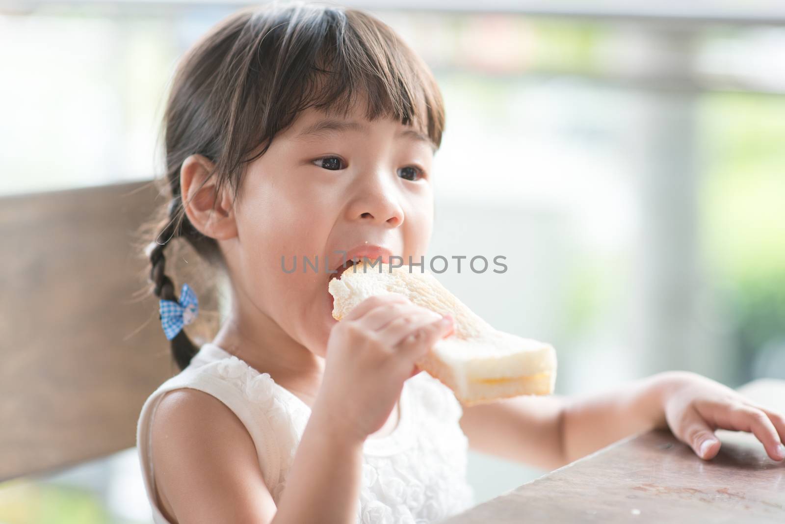 Asian child eating butter toast at cafe. Outdoor family lifestyle with natural light.