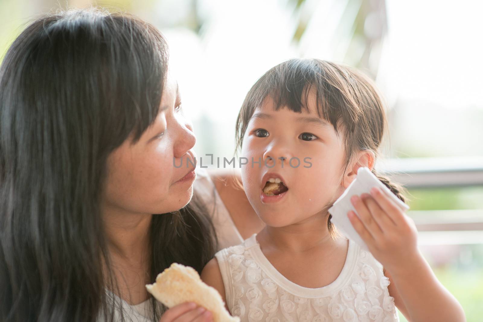 Child wipes mouth at cafe. Asian family outdoor lifestyle with natural light.