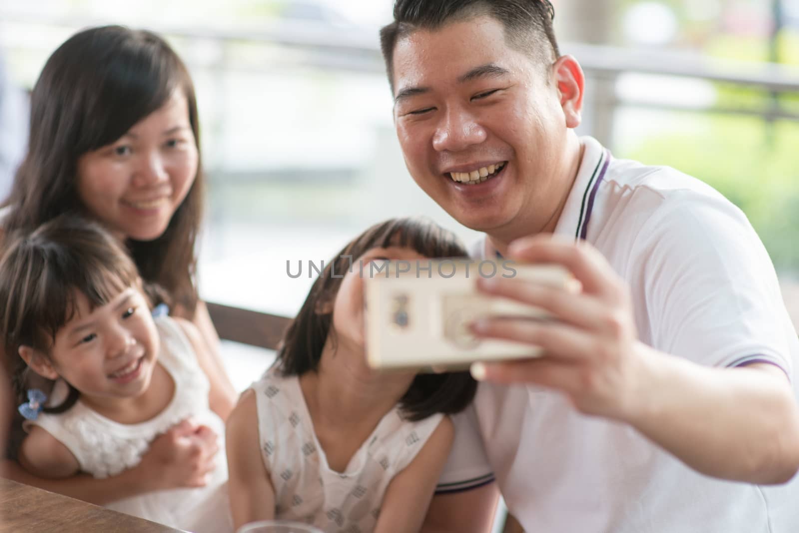 Happy Asian family taking selfie with smart phone at cafe. Outdoor lifestyle with natural light.