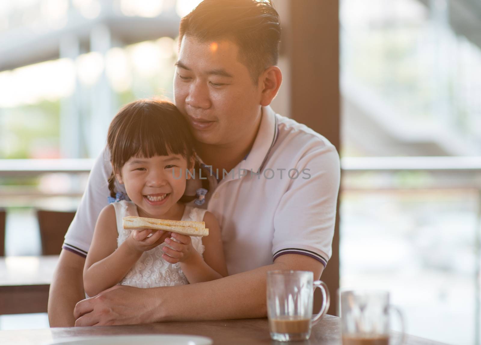 Adorable Asian child eating butter toast at cafe. Outdoor family lifestyle with natural light.