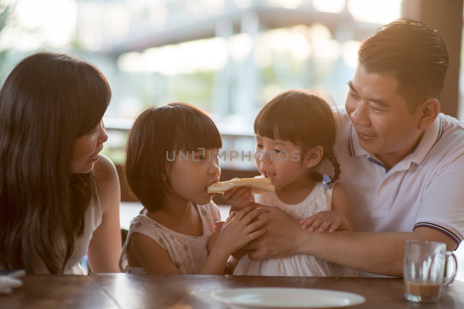 Adorable children eating and sharing butter toast at cafe. Asian family outdoor lifestyle with natural light.