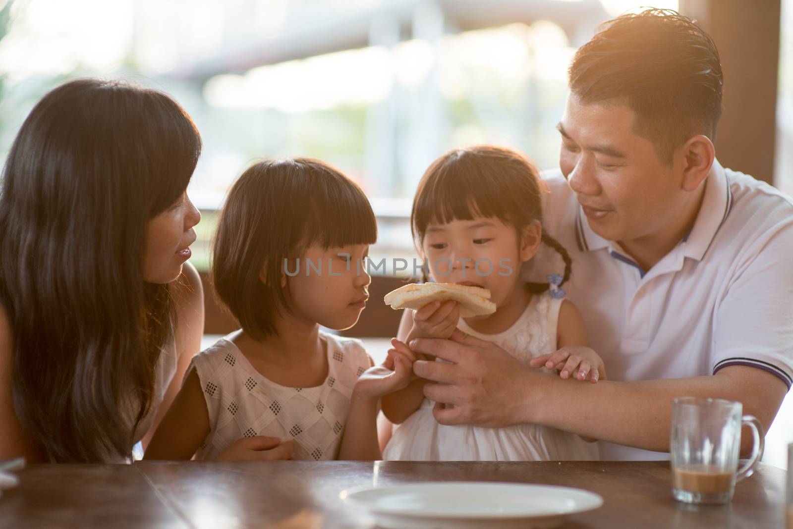 Cute children eating and sharing butter toast at cafe. Asian family outdoor lifestyle with natural light.
