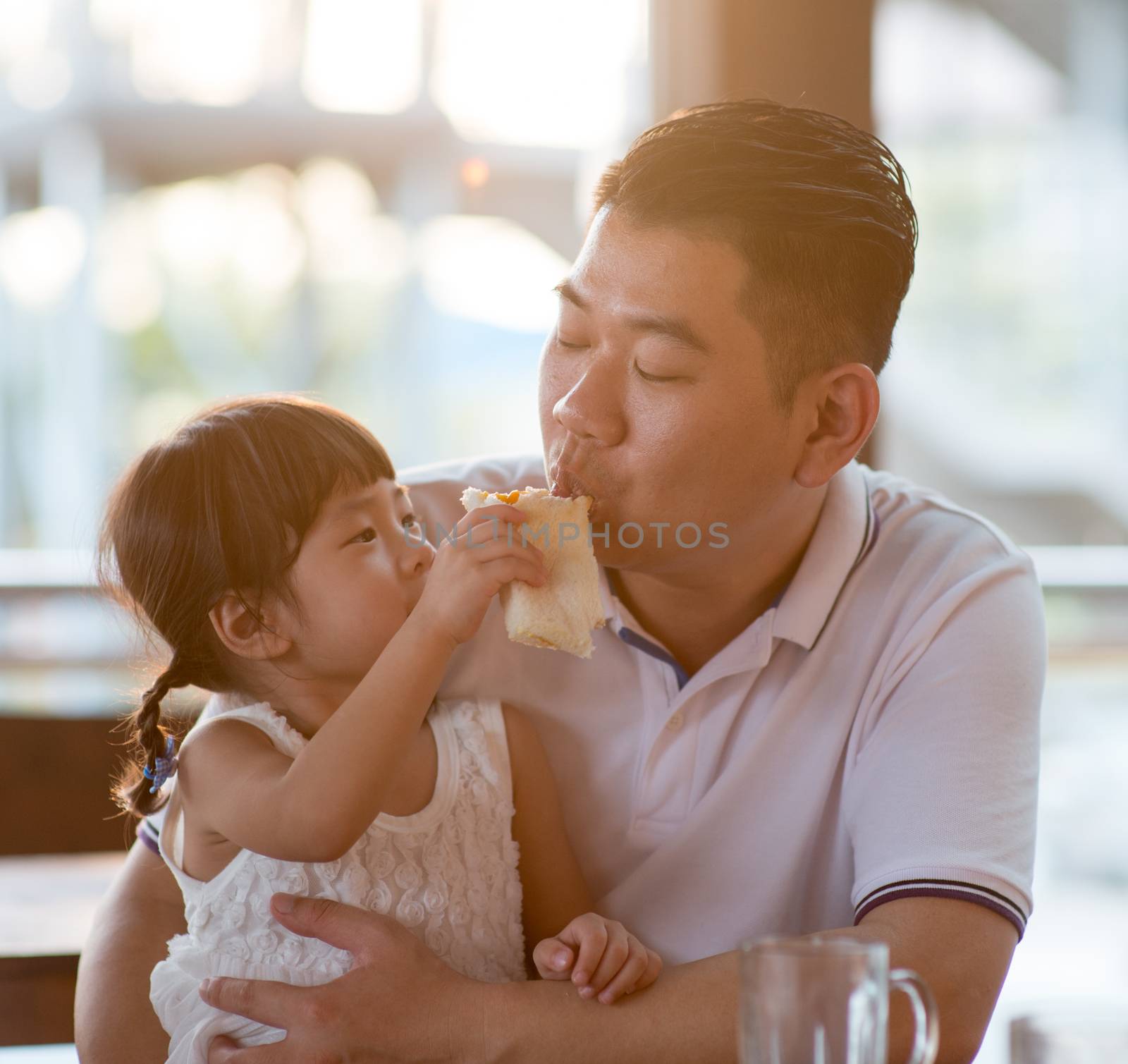 Daughter feeding bread to daddy at cafeteria. Asian family outdoor lifestyle with natural light.