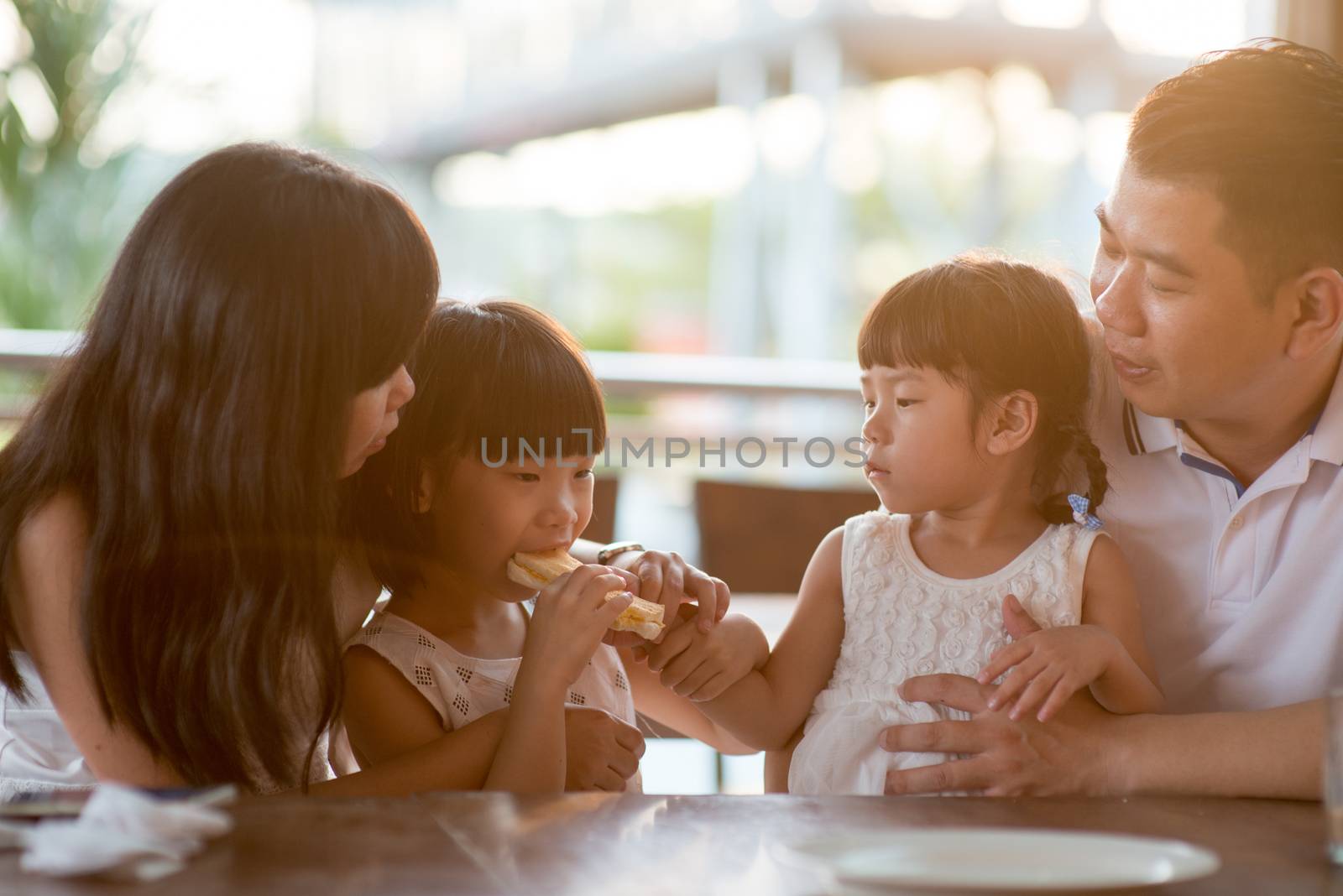 Children eating and sharing bread at cafeteria. Asian family outdoor lifestyle with natural light.
