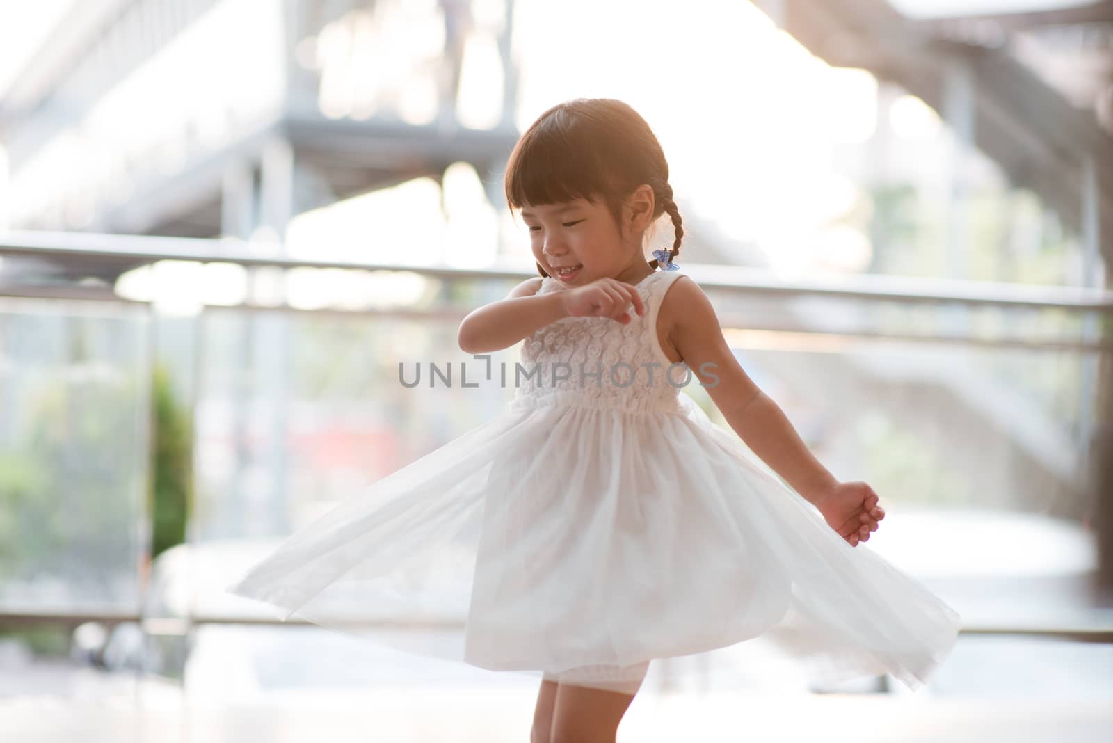 Happy adorable little girl in white dress dancing. Asian family outdoor lifestyle with natural light.